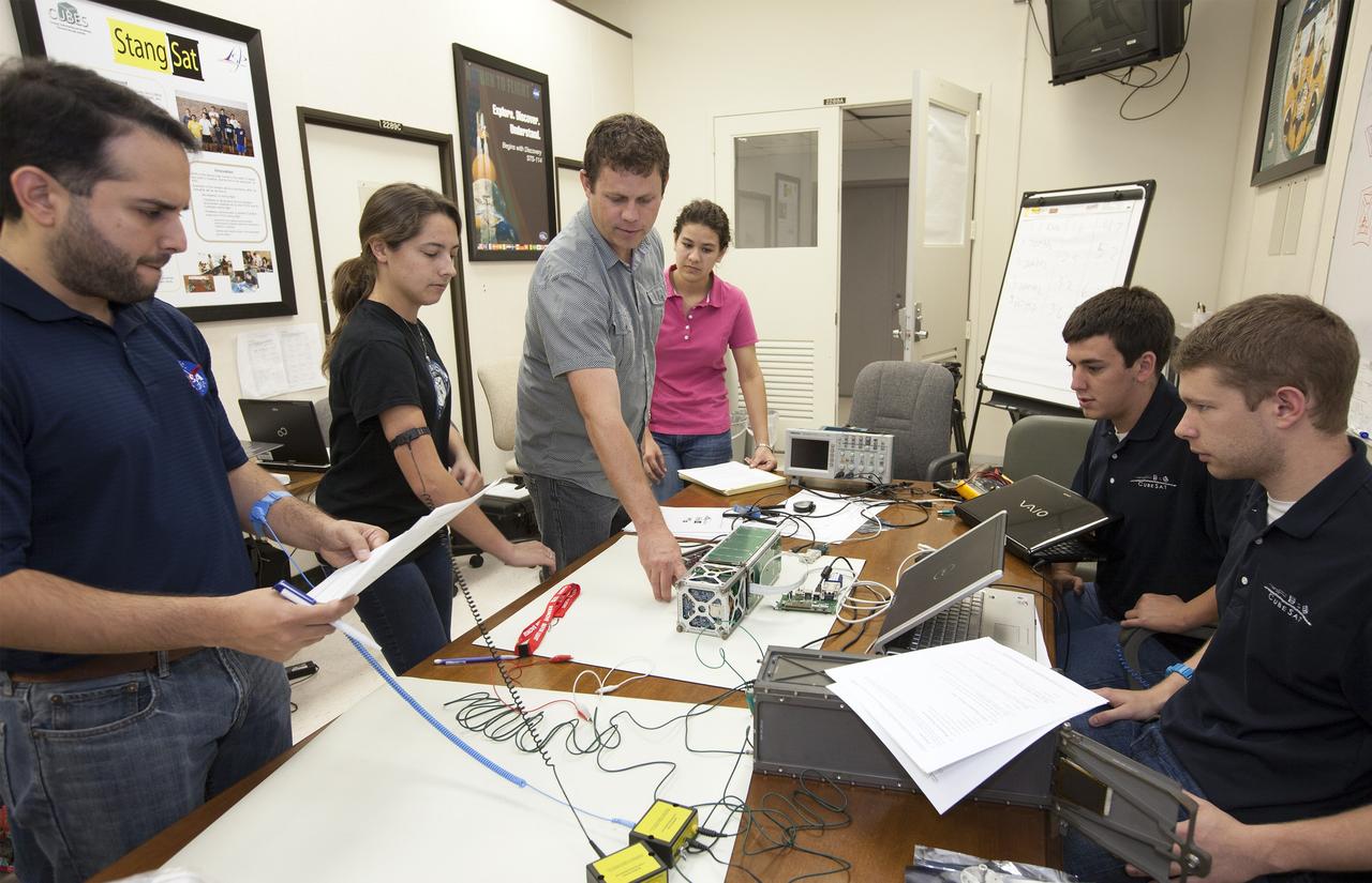 CAPE CANAVERAL, Fla. – Students from California Polytechnic Institute, or CalPoly, and Merritt Island High School in Florida perform integration tests on a pair of cubesats they will fly on a suborbital mission in the summer. A team from each school built a satellite and the two will work together inside a small rocket to measure vibration and other data during launch. NASA engineers, including Shaun Daly, in gray shirt, are acting as mentors for the project and some of the space agency's labs at Kennedy Space Center, including this one inside the Operations and Checkout Building, are being used by the teams. Photo credit: NASA/Kim Shiflett