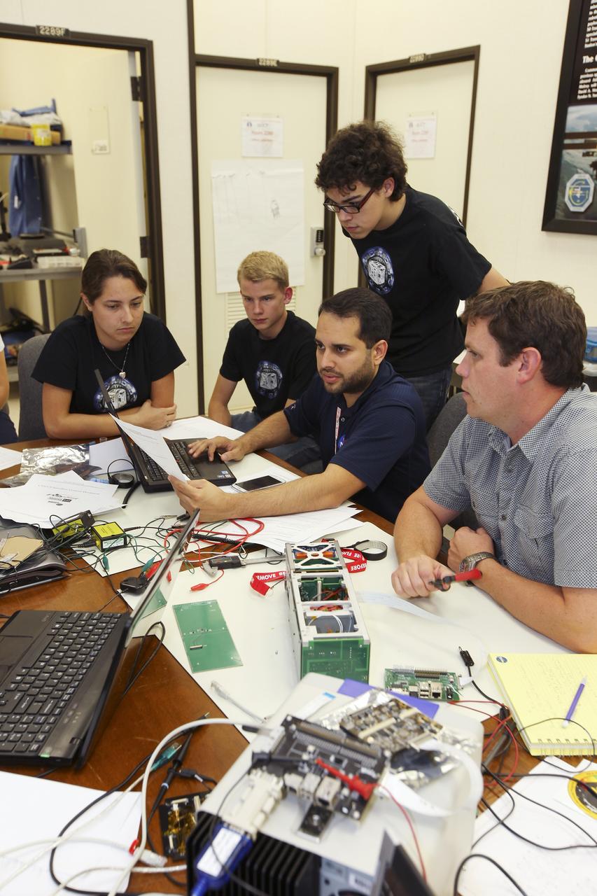 CAPE CANAVERAL, Fla. – Students from California Polytechnic Institute, or CalPoly, and Merritt Island High School in Florida perform integration tests on a pair of cubesats they will fly on a suborbital mission in the summer. A team from each school built a satellite and the two will work together inside a small rocket to measure vibration and other data during launch. NASA engineers, including Shaun Daly, in gray shirt, are acting as mentors for the project and some of the space agency's labs at Kennedy Space Center, including this one inside the Operations and Checkout Building, are being used by the teams. Photo credit: NASA/Kim Shiflett