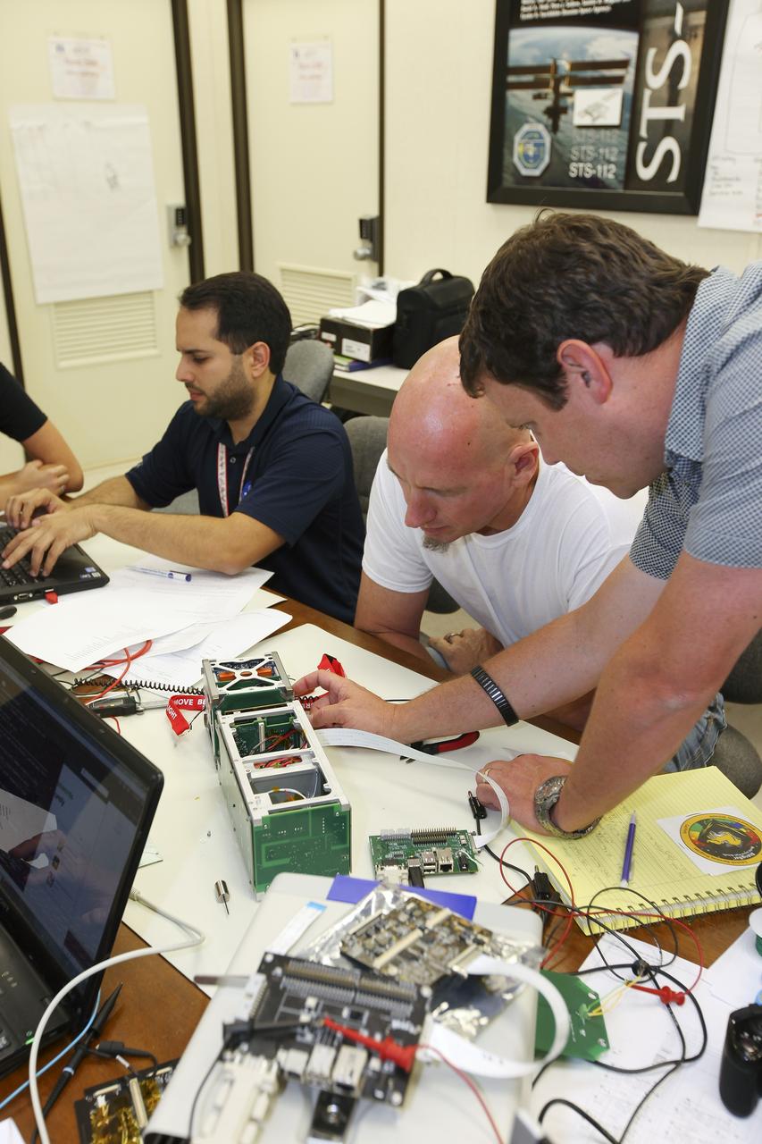 CAPE CANAVERAL, Fla. – Students from California Polytechnic Institute, or CalPoly, and Merritt Island High School in Florida perform integration tests on a pair of cubesats they will fly on a suborbital mission in the summer. A team from each school built a satellite and the two will work together inside a small rocket to measure vibration and other data during launch. NASA engineers, including Shaun Daly, in gray shirt, are acting as mentors for the project and some of the space agency's labs at Kennedy Space Center, including this one inside the Operations and Checkout Building, are being used by the teams. Photo credit: NASA/Kim Shiflett