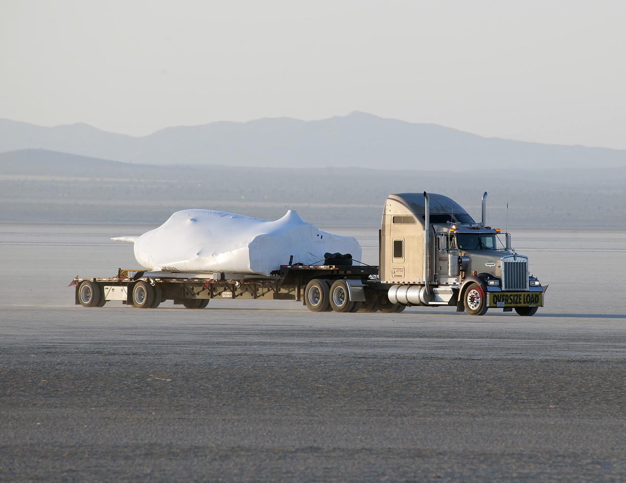 EDWARDS, Calif. – ED13-0142-01: With its wings and tail structure removed and shrouded in plastic wrap for ground transport, Sierra Nevada Corporation, or SNC, Space Systems' Dream Chaser engineering test article is hauled across the bed of Rogers Dry Lake at Edwards Air Force Base, Calif., to NASA's Dryden Flight Research Center. The Dream Chaser will begin its approach-and-landing flight test program in collaboration with NASA's Commercial Crew Program this summer.       SNC is one of three companies working with NASA's Commercial Crew Program, or CCP, during the agency's Commercial Crew Integrated Capability, or CCiCap, initiative, which is intended to lead to the availability of commercial human spaceflight services for government and commercial customers. To learn more about CCP and its industry partners, visit www.nasa.gov/commercialcrew. Image credit: NASA/Tom Tschida