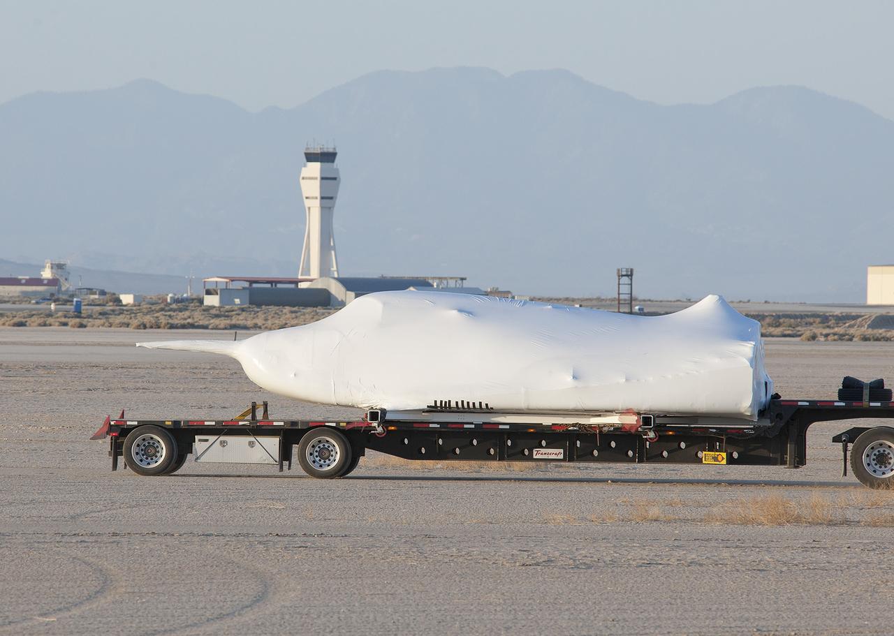 EDWARDS, Calif. – ED13-0142-03: Shrouded in plastic wrap with its wings and tail structure removed for ground transport, Sierra Nevada Corporation, or SNC, Space Systems' Dream Chaser engineering test article is hauled across the bed of Rogers Dry Lake in front of the control tower at Edwards Air Force Base, Calif., to NASA's Dryden Flight Research Center. The Dream Chaser will begin its flight test program in collaboration with NASA's Commercial Crew Program this summer.    SNC is one of three companies working with NASA's Commercial Crew Program, or CCP, during the agency's Commercial Crew Integrated Capability, or CCiCap, initiative, which is intended to lead to the availability of commercial human spaceflight services for government and commercial customers. To learn more about CCP and its industry partners, visit www.nasa.gov/commercialcrew. Image credit: NASA/Tom Tschida