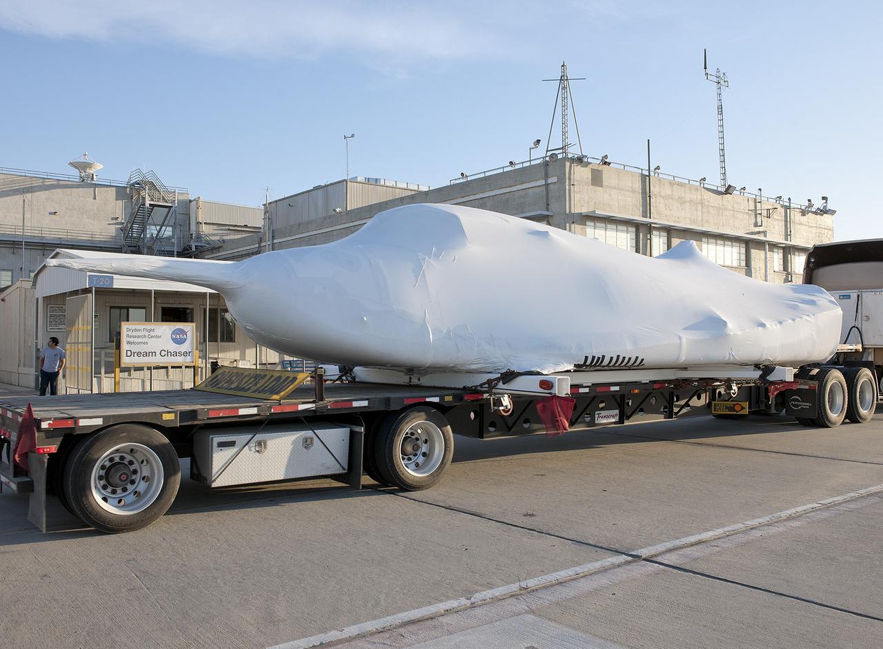 EDWARDS, Calif. – ED13-0142-10: The flatbed truck and trailer that transported Sierra Nevada Corporation, or SNC, Space Systems' Dream Chaser engineering test article pauses on the aircraft ramp at NASA's Dryden Flight Research Center on Edwards Air Force Base, Calif., upon arrival at the center. Following removal of the protective plastic wrap and reinstallation of its wings and tail structure, the Dream Chaser will begin ground tests in the next few weeks leading to approach and landing flight tests this summer.      SNC is one of three companies working with NASA's Commercial Crew Program, or CCP, during the agency's Commercial Crew Integrated Capability, or CCiCap, initiative, which is intended to lead to the availability of commercial human spaceflight services for government and commercial customers. To learn more about CCP and its industry partners, visit www.nasa.gov/commercialcrew. Image credit: NASA/Tom Tschida