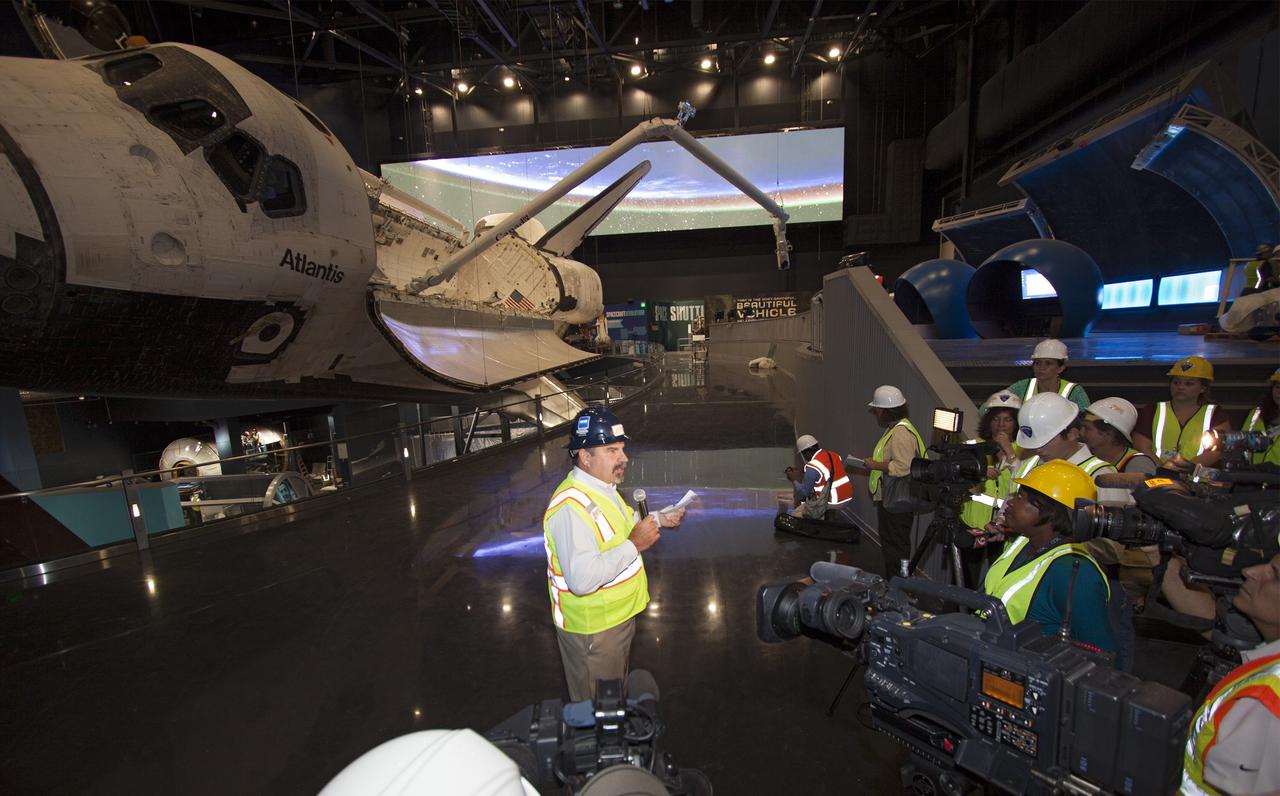 CAPE CANAVERAL, Fla. – At the Kennedy Space Center Visitor Complex in Florida, Tim Macy, the director of project development and construction for Delaware North Companies Parks & Resorts, speaks to members of the media during a tour of the new “Space Shuttle Atlantis” exhibit, a 90,000-square-foot facility, scheduled to open June 29, 2013. Behind Moore, space shuttle Atlantis’ payload bay doors are open and the orbiter has been tilted at a 43.21 angle to the portside and supported by special jacks to elevate it 26 feet from the ground. The robotic arm has been installed in the payload bay.    The new $100 million facility will include interactive exhibits that tell the story of the 30-year Space Shuttle Program and highlight the future of space exploration. Visitors to the exhibit will get an up close look at Atlantis with its payload bay doors open, similar to how it looked in space. Photo credit: NASA/Jim Grossmann