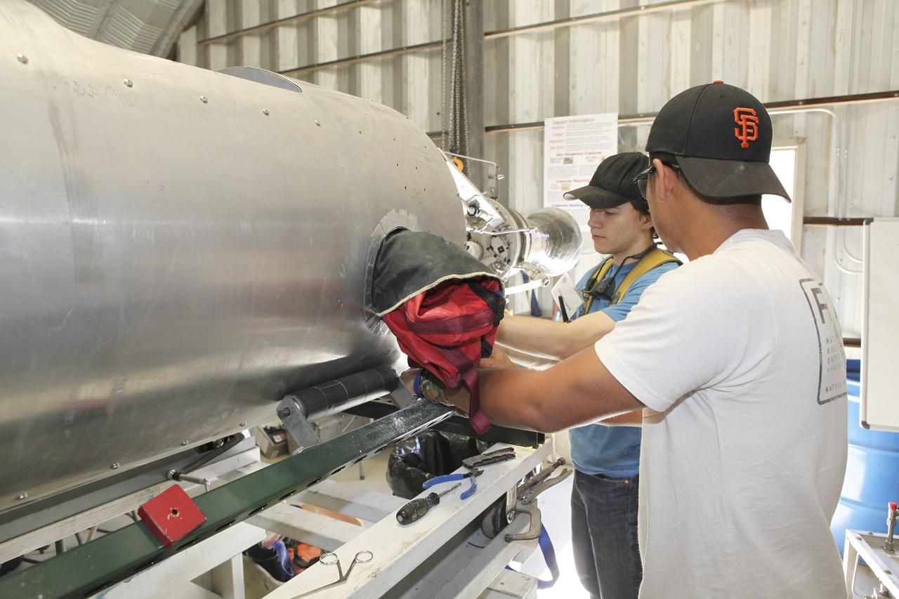 MOJAVE DESERT, Calif. – In the Mojave Desert in California, students and engineers pack the parachute in the Garvey Spacecraft Corporation's Prospector P-18D rocket. The work is in preparation for the June 15 launch of a on a high-altitude, suborbital flight. The rocket will carry four satellites made from four-inch cube section. Collectively known as CubeSats, the satellites will record shock, vibrations and heat inside the rocket. They will not be released during the test flight, but the results will be used to prove or strengthen their designs before they are carried into orbit in 2014 on a much larger rocket. A new, lightweight carrier is also being tested for use on future missions to deploy the small spacecraft. The flight also is being watched closely as a model for trying out new or off-the-shelf technologies quickly before putting them in the pipeline for use on NASA's largest launchers. Built by several different organizations, including a university, a NASA field center and a high school, the spacecraft are four-inch cubes designed to fly on their own eventually, but will remain firmly attached to the rocket during the upcoming mission. For more information, visit http://www.nasa.gov/mission_pages/smallsats/elana/cubesatlaunchpreview.html Photo credit: NASA/Dimitri Gerondidakis