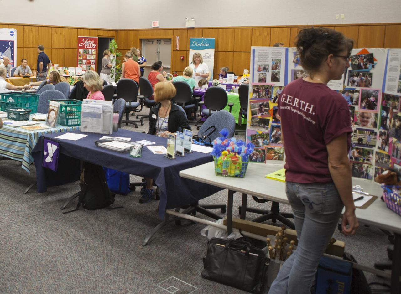 CAPE CANAVERAL, Fla. – Linnea Applegate, right, of Grace Equine Rescue and Therapy for Humans, or GERTH, organizes her booth during the National Employee Health and Fitness Day event in the Operations and Checkout Building's Mission Briefing Room. GERTH is a nonprofit organization in Cocoa, Fla., that brings horses, children and adults together in a safe, nurturing and healing environment to promote therapeutic healing. Other vendors shown in the background include Bridget Griffin of the YMCA of Titusville, center, and Sunseed Co-op’s Marcia Cooney, in pink. Photo credit: NASA/Daniel Casper