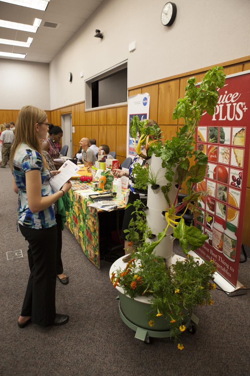 CAPE CANAVERAL, Fla. – A Kennedy Space Center worker talks with Rikki Eloian, of Juice Plus, hidden behind the plant, during the National Employee Health and Fitness Day event in the Operations and Checkout Building's Mission Briefing Room. Other vendors represented at the event included the American Cancer Society, Running Zone and Parrish Medical Center Diabetes Program. Photo credit: NASA/Daniel Casper