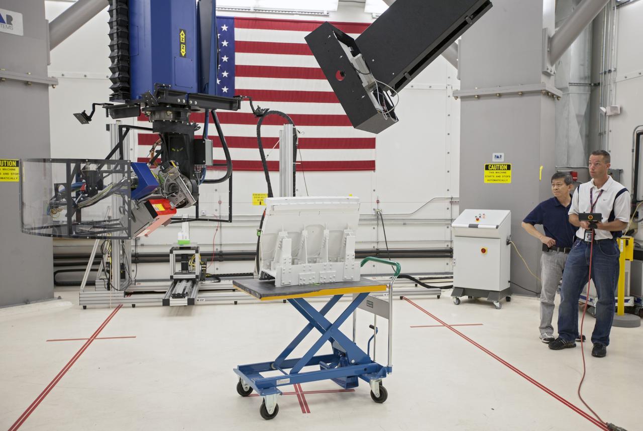 CAPE CANAVERAL, Fla. – In Hangar N at Cape Canaveral Air Force Station, PaR Systems, Inc. development engineer Wayne Cheng, left, and operations engineer Jeff Elston operate a robotic system used in nondestructive testing. The 11-axis robotic system takes X-ray images of hardware for evaluation.      NASA's Kennedy Space Center in Florida recently established a partnership agreement with PaR Systems, Inc. of Shoreview, Minn., for operation of the Hangar N facility and its nondestructive testing and evaluation equipment. As the spaceport transitions from a historically government-only launch facility to a multi-user spaceport for both federal and commercial customers, partnerships between the space agency and other organizations will be a key element in that effort. Hangar N is located at Cape Canaveral Air Force Station adjacent to Kennedy and houses a unique inventory of test and evaluation equipment and the capability for current and future mission spaceflight support. Photo credit: NASA/ Dimitri Gerondidakis