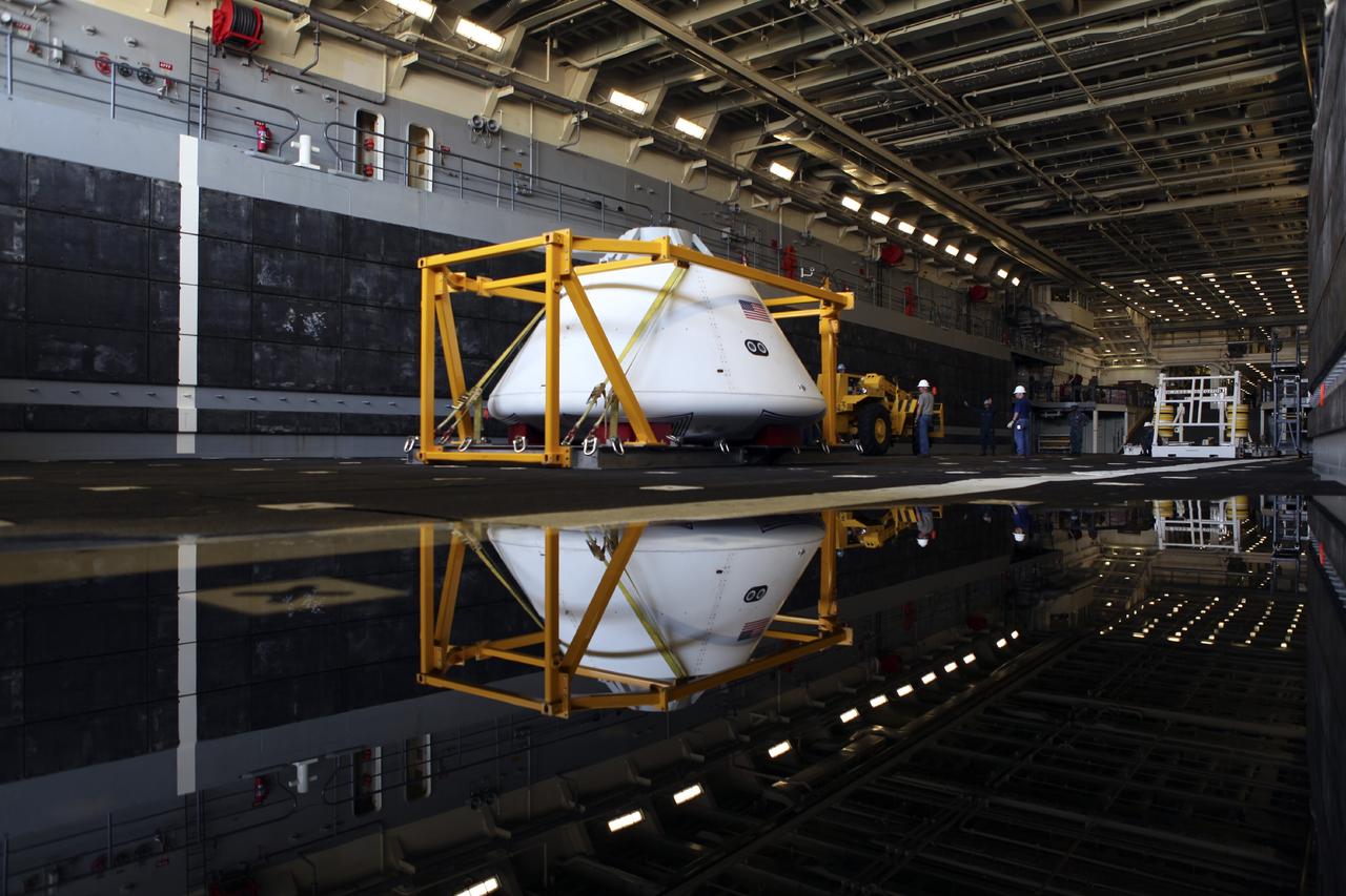 HAMPTON, Va. – At the Naval Station Norfolk near NASA’s Langley Research Center in Virginia, the Orion boilerplate test article is reflected in water on a U.S. Navy ship. The test article and support equipment for a stationary recovery test were transferred to the ship from a floating dock system. NASA and the U.S. Navy are conducting tests to prepare for recovery of the Orion crew module and forward bay cover on its return from a deep space mission. The stationary recovery test will allow the teams to demonstrate and evaluate the recovery processes, procedures, hardware and personnel in a controlled environment before conducting a second recovery test next year in open waters. Orion is the exploration spacecraft designed to carry astronauts to destinations not yet explored by humans, including an asteroid and Mars. It will have emergency abort capability, sustain the crew during space travel and provide safe re-entry from deep space return velocities. The first unpiloted test flight of the Orion is scheduled to launch in 2014 atop a Delta IV rocket and in 2017 on NASA’s Space Launch System rocket. For more information, visit http://www.nasa.gov/orion. Photo credit: NASA/Dimitri Gerondidakis