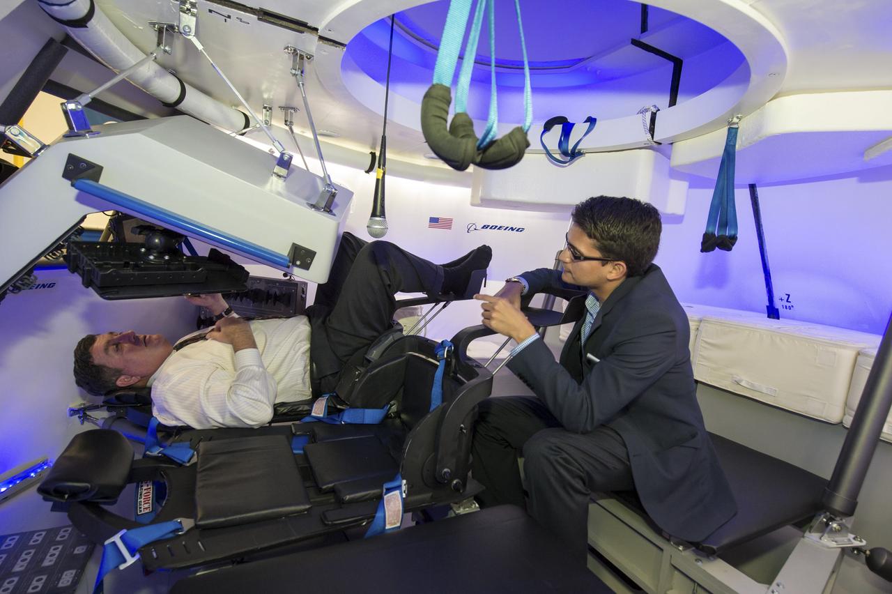 HOUSTON -- JSC-2013-E076056 -- Kirk Shireman, deputy director of NASA's Johnson Space Center, takes the controls of The Boeing Company's mock-up CST-100 spacecraft at the company's Houston Product Support Center. Helping Shireman inside the fully outfitted test version of the CST-100 is Tony Castilleja, a mechanical engineer working on the Boeing project. Boeing showcased its work on a fully outfitted test version of the spacecraft to Bolden and Johnson management.    Boeing's CST-100 is designed to transport a mix of crew and cargo to low-Earth-orbit destinations. Boeing is one of three aerospace industry partners working with NASA's Commercial Crew Program, or CCP, during the Commercial Crew Integrated Capability, or CCiCap, initiative, which is intended to make commercial human spaceflight services available for government and commercial customers. To learn more about CCP, visit www.nasa.gov/commercialcrew. Photo credit: NASA/James Blair