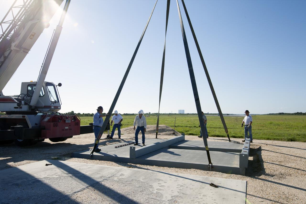 CAPE CANAVERAL, Fla. - At NASA’s Kennedy Space Center in Florida, workers position the movable launch platform for the Project Morpheus lander in its new site adjacent to a hazard field created to support the project at the north end of the Shuttle Landing Facility, or SLF. In the distance is the 525-foot-tall Vehicle Assembly Building.    Testing of the prototype lander has been ongoing at NASA’s Johnson Space Center in Houston in preparation for free flight. The lander is scheduled for delivery to Kennedy in October. The SLF will provide the lander with the kind of field necessary for realistic testing, complete with rocks, craters and hazards to avoid. Morpheus utilizes an autonomous landing and hazard avoidance technology, or ALHAT, payload that will allow it to navigate to clear landing sites amidst obstacles during its descent. Project Morpheus is one of 20 small projects comprising the Advanced Exploration Systems, or AES, program in NASA’s Human Exploration and Operations Mission Directorate. AES projects pioneer new approaches for rapidly developing prototype systems, demonstrating key capabilities and validating operational concepts for future human missions beyond Earth orbit. For more information on Project Morpheus, visit http://www.nasa.gov/centers/johnson/exploration/morpheus/index.html. Photo credit: NASA/Kim Shiflett