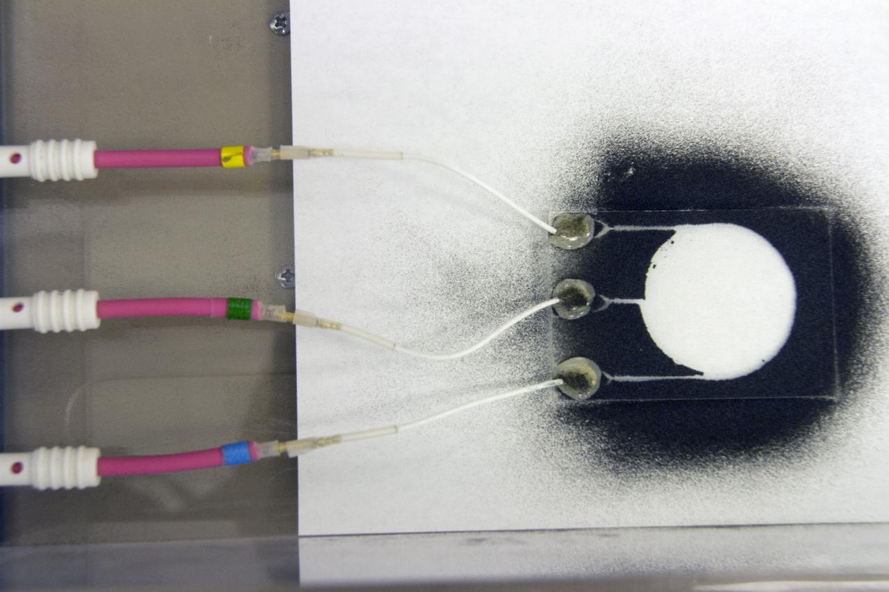 CAPE CANAVERAL, Fla. -- Dust particles scatter during an experiment for the Electrodynamic Dust Shield for Dust Mitigation project in the Electrostatics and Surface Physics Laboratory in the SwampWorks at NASA's Kennedy Space Center in Florida. The fabricated material is designed to mimic the dust on the lunar surface. The technology works by creating an electric field that propagates out like the ripples on a pond. This could prevent dust accumulation on spacesuits, thermal radiators, solar panels, optical instruments and view ports for future lunar and Mars exploration activities. CAPE CANAVERAL, Fla. -- Preparations are underway to conduct a dust particle experiment for the Electrodynamic Dust Shield for Dust Mitigation project in the Electrostatics and Surface Physics Laboratory in the SwampWorks at NASA's Kennedy Space Center in Florida. The technology works by creating an electric field that propagates out like the ripples on a pond. This could prevent dust accumulation on spacesuits, thermal radiators, solar panels, optical instruments and view ports for future lunar and Mars exploration activities.