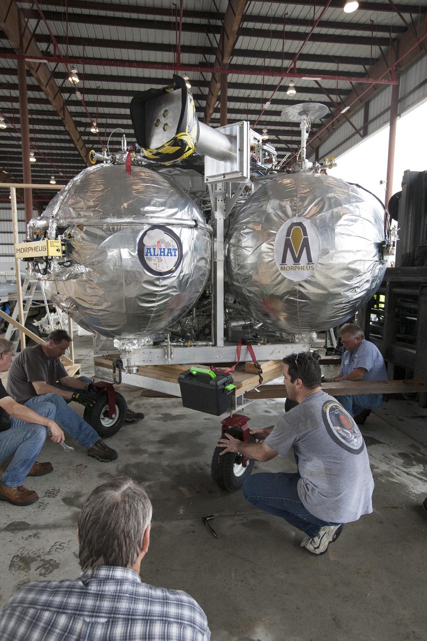 CAPE CANAVERAL, Fla. -- At NASA’s Kennedy Space Center in Florida, technicians position the Project Morpheus lander onto a transporter inside a support building at the Shuttle Landing Facility, or SLF. Testing of the prototype lander has been ongoing at NASA’s Johnson Space Center in Houston in preparation for free flight testing at Kennedy. The SLF will provide the lander with the kind of field necessary for realistic testing, complete with rocks, craters and hazards to avoid. Morpheus utilizes an autonomous landing and hazard avoidance technology, or ALHAT, payload that will allow it to navigate to clear landing sites amidst rocks, craters and other hazards during its descent. Project Morpheus is one of 20 small projects comprising the Advanced Exploration Systems, or AES, program in NASA’s Human Exploration and Operations Mission Directorate. AES projects pioneer new approaches for rapidly developing prototype systems, demonstrating key capabilities and validating operational concepts for future human missions beyond Earth orbit. For more information on Project Morpheus, visit http://www.nasa.gov/centers/johnson/exploration/morpheus/index.html. Photo credit: NASA/Kim Shiflett