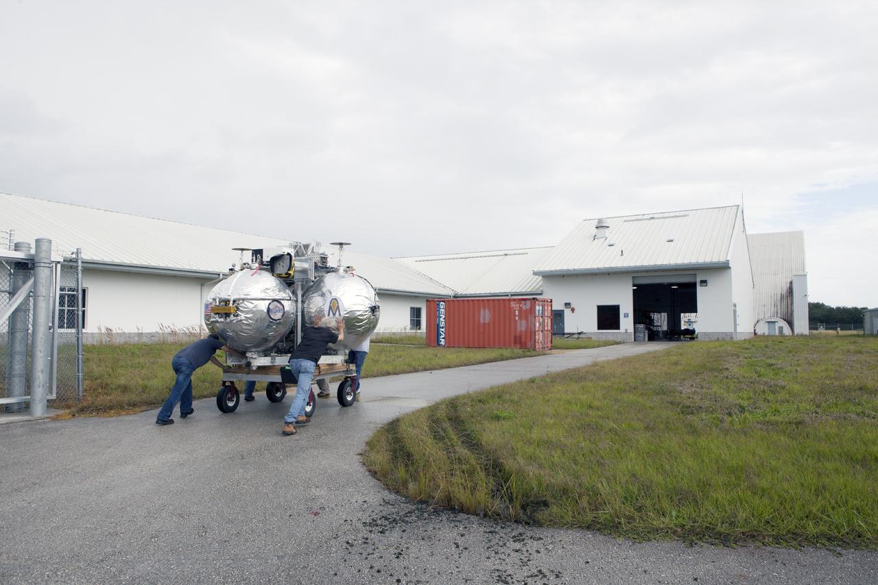 CAPE CANAVERAL, Fla. -- At NASA’s Kennedy Space Center in Florida, technicians move the Project Morpheus lander on a small transporter to a support building at the Shuttle Landing Facility, or SLF. Testing of the prototype lander has been ongoing at NASA’s Johnson Space Center in Houston in preparation for free flight testing at Kennedy. The SLF will provide the lander with the kind of field necessary for realistic testing, complete with rocks, craters and hazards to avoid. Morpheus utilizes an autonomous landing and hazard avoidance technology, or ALHAT, payload that will allow it to navigate to clear landing sites amidst rocks, craters and other hazards during its descent. Project Morpheus is one of 20 small projects comprising the Advanced Exploration Systems, or AES, program in NASA’s Human Exploration and Operations Mission Directorate. AES projects pioneer new approaches for rapidly developing prototype systems, demonstrating key capabilities and validating operational concepts for future human missions beyond Earth orbit. For more information on Project Morpheus, visit http://www.nasa.gov/centers/johnson/exploration/morpheus/index.html. Photo credit: NASA/Kim Shiflett