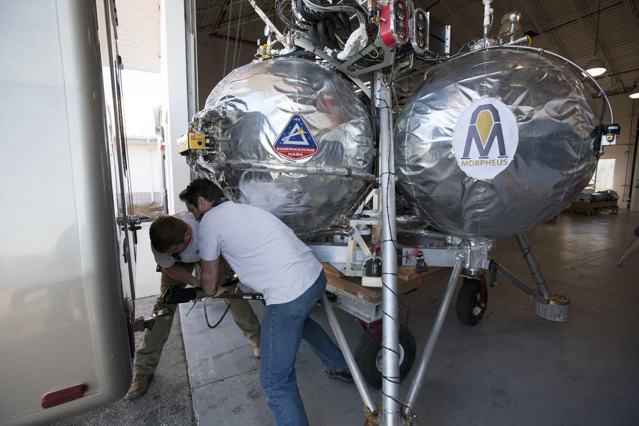 CAPE CANAVERAL, Fla. -- At NASA’s Kennedy Space Center in Florida, technicians prepare the Project Morpheus prototype lander to be transported from a support building to a launch platform at the north end of the Shuttle Landing Facility. Testing of the prototype lander was performed at NASA’s Johnson Space Center in Houston in preparation for tethered and free flight testing at Kennedy.    The landing facility will provide the lander with the kind of field necessary for realistic testing, complete with rocks, craters and hazards to avoid. Morpheus utilizes an autonomous landing and hazard avoidance technology, or ALHAT, payload that will allow it to navigate to clear landing sites amidst rocks, craters and other hazards during its descent. Project Morpheus is being managed under the Advanced Exploration Systems, or AES, Division in NASA’s Human Exploration and Operations Mission Directorate. The efforts in AES pioneer new approaches for rapidly developing prototype systems, demonstrating key capabilities and validating operational concepts for future human missions beyond Earth orbit. For more information on Project Morpheus, visit http://morpheuslander.jsc.nasa.gov.  Photo credit: NASA/Kim Shiflett