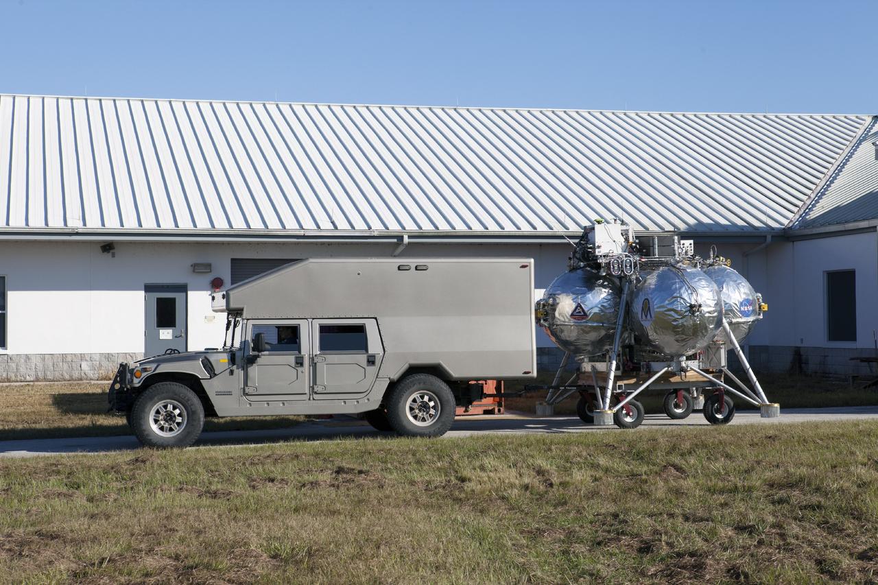 CAPE CANAVERAL, Fla. -- At NASA’s Kennedy Space Center in Florida, the Project Morpheus prototype lander is prepared for its move from a support building to a launch platform at the north end of the Shuttle Landing Facility. Testing of the prototype lander was performed at NASA’s Johnson Space Center in Houston in preparation for tethered and free flight testing at Kennedy.    The landing facility will provide the lander with the kind of field necessary for realistic testing, complete with rocks, craters and hazards to avoid. Morpheus utilizes an autonomous landing and hazard avoidance technology, or ALHAT, payload that will allow it to navigate to clear landing sites amidst rocks, craters and other hazards during its descent. Project Morpheus is being managed under the Advanced Exploration Systems, or AES, Division in NASA’s Human Exploration and Operations Mission Directorate. The efforts in AES pioneer new approaches for rapidly developing prototype systems, demonstrating key capabilities and validating operational concepts for future human missions beyond Earth orbit. For more information on Project Morpheus, visit http://morpheuslander.jsc.nasa.gov.  Photo credit: NASA/Kim Shiflett