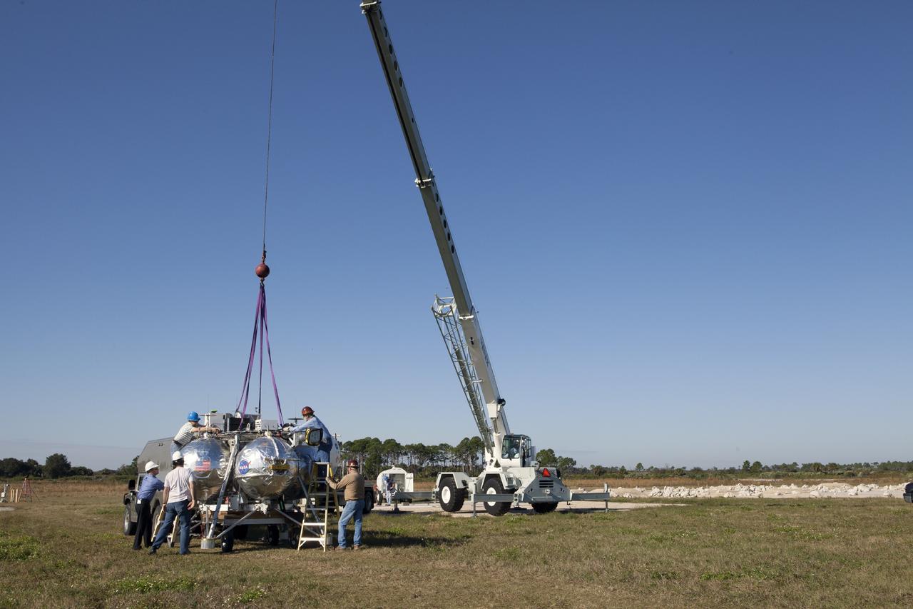 CAPE CANAVERAL, Fla. -- At NASA’s Kennedy Space Center in Florida, a team of engineers and technicians attaches a tether to the Project Morpheus prototype lander near the north end of the Shuttle Landing Facility. Testing of the prototype lander was performed at NASA’s Johnson Space Center in Houston in preparation for Morpheus’ tethered and free flight testing at Kennedy. The landing facility will provide the lander with the kind of field necessary for realistic testing, complete with rocks, craters and hazards to avoid. Morpheus utilizes an autonomous landing and hazard avoidance technology, or ALHAT, payload that will allow it to navigate to clear landing sites amidst rocks, craters and other hazards during its descent. Project Morpheus is being managed under the Advanced Exploration Systems, or AES, Division in NASA’s Human Exploration and Operations Mission Directorate. The efforts in AES pioneer new approaches for rapidly developing prototype systems, demonstrating key capabilities and validating operational concepts for future human missions beyond Earth orbit. For more information on Project Morpheus, visit http://morpheuslander.jsc.nasa.gov. Photo credit: NASA/Kim Shiflett