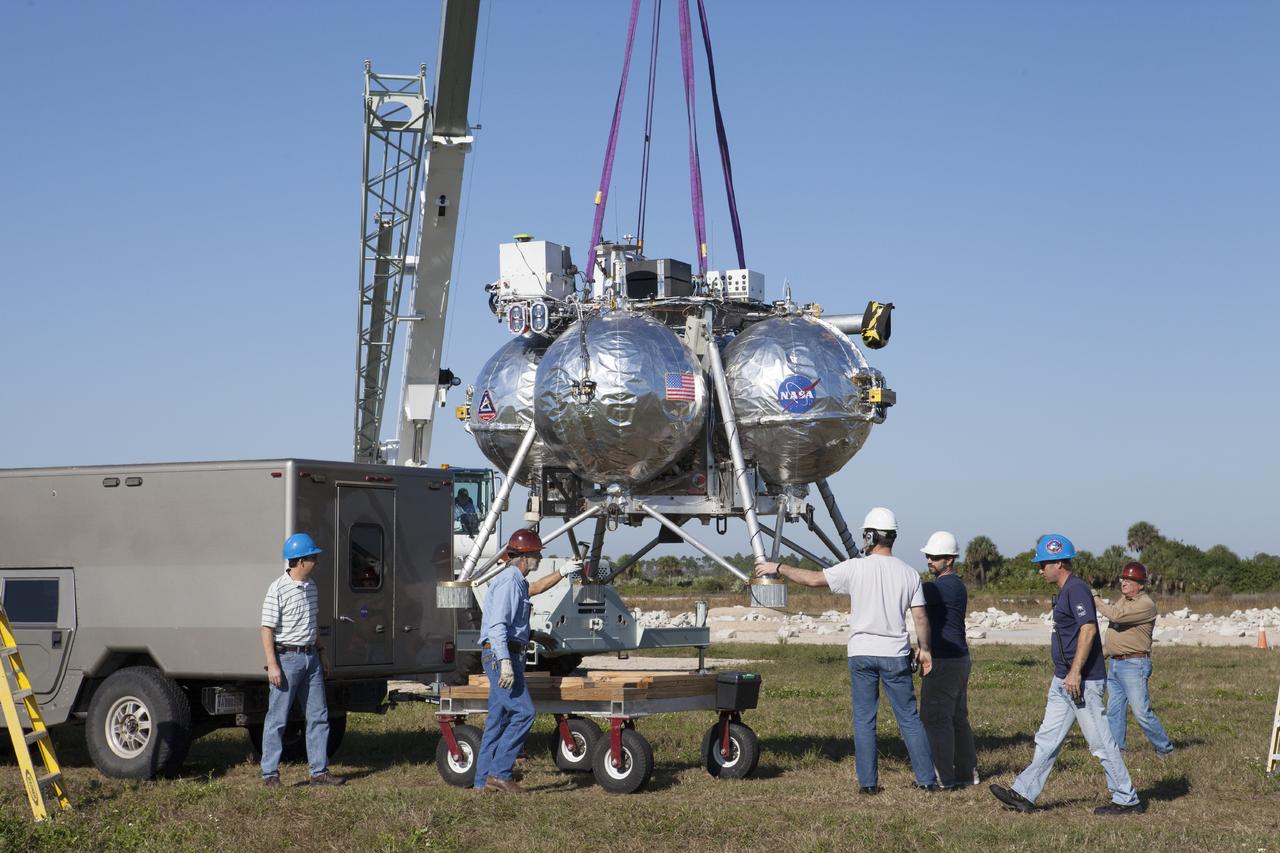 CAPE CANAVERAL, Fla. -- At NASA’s Kennedy Space Center in Florida, a team of engineers and technicians assist as a tether is used to move the Project Morpheus prototype lander to a launch platform at the north end of the Shuttle Landing Facility. Testing of the prototype lander has been ongoing at NASA’s Johnson Space Center in Houston in preparation for tethered and free flight testing at Kennedy.    The landing facility will provide the lander with the kind of field necessary for realistic testing, complete with rocks, craters and hazards to avoid. Morpheus utilizes an autonomous landing and hazard avoidance technology, or ALHAT, payload that will allow it to navigate to clear landing sites amidst rocks, craters and other hazards during its descent. Project Morpheus is being managed under the Advanced Exploration Systems, or AES, Division in NASA’s Human Exploration and Operations Mission Directorate. The efforts in AES pioneer new approaches for rapidly developing prototype systems, demonstrating key capabilities and validating operational concepts for future human missions beyond Earth orbit. For more information on Project Morpheus, visit http://morpheuslander.jsc.nasa.gov.  Photo credit: NASA/Kim Shiflett