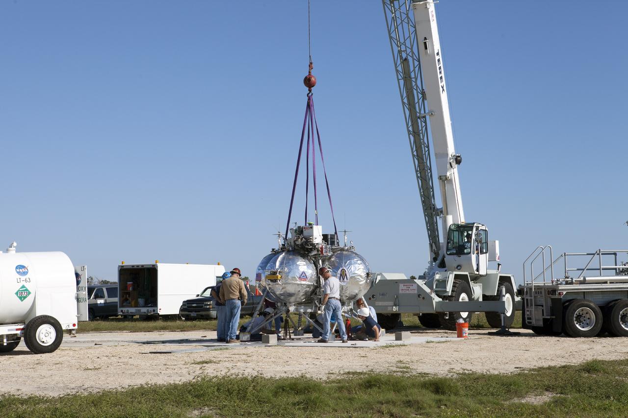 CAPE CANAVERAL, Fla. -- At NASA’s Kennedy Space Center in Florida, a team of engineers and technicians assist as a tether is used to lower the Project Morpheus prototype lander onto a launch platform at the north end of the Shuttle Landing Facility. Testing of the prototype lander has been ongoing at NASA’s Johnson Space Center in Houston in preparation for tethered and free flight testing at Kennedy. The landing facility will provide the lander with the kind of field necessary for realistic testing, complete with rocks, craters and hazards to avoid. Morpheus utilizes an autonomous landing and hazard avoidance technology, or ALHAT, payload that will allow it to navigate to clear landing sites amidst rocks, craters and other hazards during its descent. Project Morpheus is being managed under the Advanced Exploration Systems, or AES, Division in NASA’s Human Exploration and Operations Mission Directorate. The efforts in AES pioneer new approaches for rapidly developing prototype systems, demonstrating key capabilities and validating operational concepts for future human missions beyond Earth orbit. For more information on Project Morpheus, visit http://morpheuslander.jsc.nasa.gov. Photo credit: NASA/Kim Shiflett