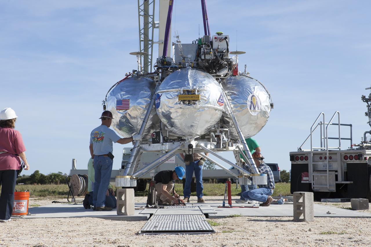 CAPE CANAVERAL, Fla. – The Project Morpheus prototype lander is attached to a tether at the launch platform located at the north end of the Shuttle Landing Facility at NASA’s Kennedy Space Center in Florida. Morpheus is being prepared for a dress rehearsal of a tethered flight test. Testing of the prototype lander was performed at NASA’s Johnson Space Center in Houston in preparation for tethered and free flight testing at Kennedy. The landing facility will provide the lander with the kind of field necessary for realistic testing, complete with rocks, craters and hazards to avoid. Morpheus utilizes an autonomous landing and hazard avoidance technology, or ALHAT, payload that will allow it to navigate to clear landing sites amidst rocks, craters and other hazards during its descent. Project Morpheus is being managed under the Advanced Exploration Systems, or AES, Division in NASA’s Human Exploration and Operations Mission Directorate. The efforts in AES pioneer new approaches for rapidly developing prototype systems, demonstrating key capabilities and validating operational concepts for future human missions beyond Earth orbit. For more information on Project Morpheus, visit http://morpheuslander.jsc.nasa.gov. Photo credit: NASA/Kim Shiflett