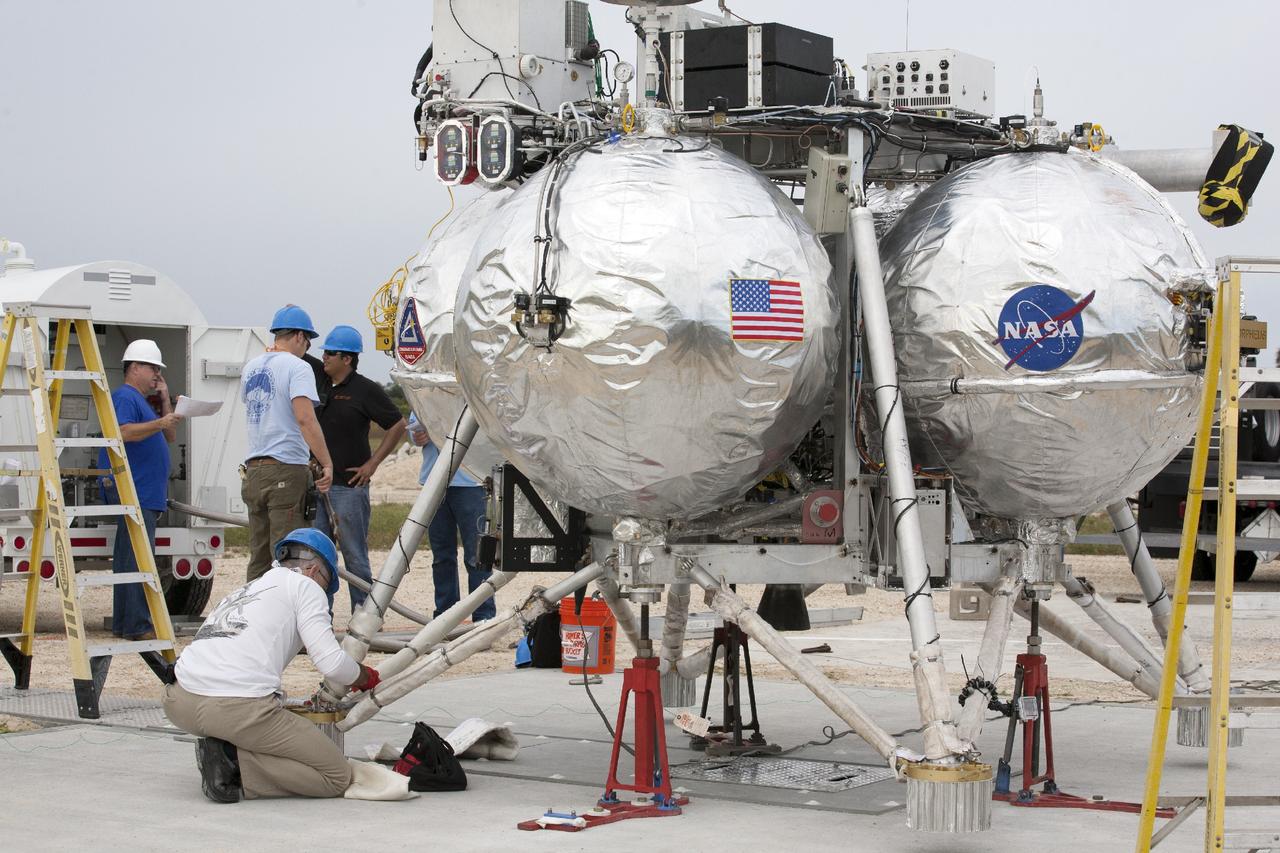 CAPE CANAVERAL, Fla. – At NASA’s Kennedy Space Center in Florida, technicians and engineers assist as the Project Morpheus prototype lander is attached to a tether and lowered onto a transportable launch platform positioned at the north end of the Shuttle Landing Facility. The lander will be prepared for a tethered test that includes lifting it 20 feet by crane, ascending another 10 feet, maneuvering backwards 10 feet, and then flying forward and descending to its original position, landing at the end of the tether. Testing of the prototype lander was performed at NASA’s Johnson Space Center in Houston in preparation for tethered and free flight testing at Kennedy. The landing facility will provide the lander with the kind of field necessary for realistic testing, complete with rocks, craters and hazards to avoid. Morpheus utilizes an autonomous landing and hazard avoidance technology, or ALHAT, payload that will allow it to navigate to clear landing sites amidst rocks, craters and other hazards during its descent. Project Morpheus is being managed under the Advanced Exploration Systems, or AES, Division in NASA’s Human Exploration and Operations Mission Directorate. The efforts in AES pioneer new approaches for rapidly developing prototype systems, demonstrating key capabilities and validating operational concepts for future human missions beyond Earth orbit. For more information on Project Morpheus, visit http://morpheuslander.jsc.nasa.gov. Photo credit: NASA/Kim Shiflett