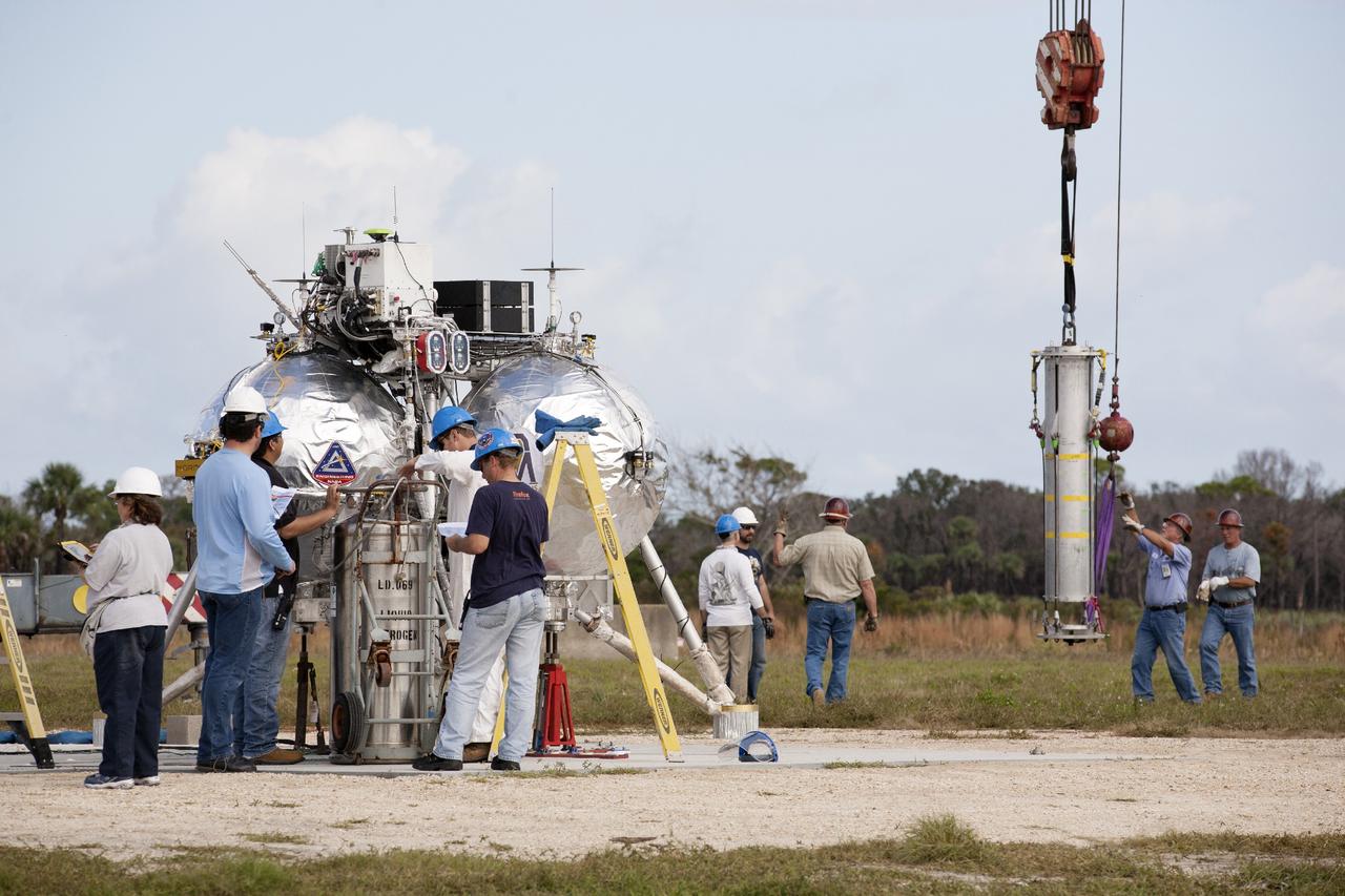 CAPE CANAVERAL, Fla. – At NASA’s Kennedy Space Center in Florida, technicians and engineers check the Project Morpheus prototype lander which has been positioned on a transportable launch platform at the north end of the Shuttle Landing Facility. The lander will be prepared for a tethered test that includes lifting it 20 feet by crane, ascending another 10 feet, maneuvering backwards 10 feet, and then flying forward and descending to its original position, landing at the end of the tether. Testing of the prototype lander was performed at NASA’s Johnson Space Center in Houston in preparation for tethered and free flight testing at Kennedy. The landing facility will provide the lander with the kind of field necessary for realistic testing, complete with rocks, craters and hazards to avoid. Morpheus utilizes an autonomous landing and hazard avoidance technology, or ALHAT, payload that will allow it to navigate to clear landing sites amidst rocks, craters and other hazards during its descent. Project Morpheus is being managed under the Advanced Exploration Systems, or AES, Division in NASA’s Human Exploration and Operations Mission Directorate. The efforts in AES pioneer new approaches for rapidly developing prototype systems, demonstrating key capabilities and validating operational concepts for future human missions beyond Earth orbit. For more information on Project Morpheus, visit http://morpheuslander.jsc.nasa.gov. Photo credit: NASA/Kim Shiflett