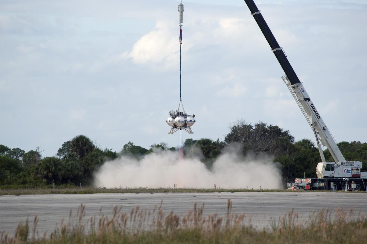 CAPE CANAVERAL, Fla. – At NASA’s Kennedy Space Center in Florida, the Project Morpheus prototype lander’s engine begins to fire during a tether test at the north end of the Shuttle Landing Facility. During the test, the lander is lifted 20 feet by crane, and will ascend another 10 feet, maneuver backwards 10 feet, and then fly forward and descend to its original position, landing at the end of the tether onto a transportable launch platform. Testing of the prototype lander was performed at NASA’s Johnson Space Center in Houston in preparation for tethered and free flight testing at Kennedy. The landing facility will provide the lander with the kind of field necessary for realistic testing, complete with rocks, craters and hazards to avoid. Morpheus utilizes an autonomous landing and hazard avoidance technology, or ALHAT, payload that will allow it to navigate to clear landing sites amidst rocks, craters and other hazards during its descent. Project Morpheus is being managed under the Advanced Exploration Systems, or AES, Division in NASA’s Human Exploration and Operations Mission Directorate. The efforts in AES pioneer new approaches for rapidly developing prototype systems, demonstrating key capabilities and validating operational concepts for future human missions beyond Earth orbit. For more information on Project Morpheus, visit http://morpheuslander.jsc.nasa.gov. Photo credit: NASA/Daniel Casper
