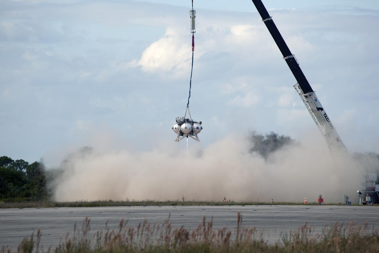 CAPE CANAVERAL, Fla. – At NASA’s Kennedy Space Center in Florida, smoke fills the air as the Project Morpheus prototype lander’s engine fires during a tether test at the north end of the Shuttle Landing Facility. During the test, the lander is lifted 20 feet by crane, and will ascend another 10 feet, maneuver backwards 10 feet, and then fly forward and descend to its original position, landing at the end of the tether onto a transportable launch platform. Testing of the prototype lander was performed at NASA’s Johnson Space Center in Houston in preparation for tethered and free flight testing at Kennedy.    The landing facility will provide the lander with the kind of field necessary for realistic testing, complete with rocks, craters and hazards to avoid. Morpheus utilizes an autonomous landing and hazard avoidance technology, or ALHAT, payload that will allow it to navigate to clear landing sites amidst rocks, craters and other hazards during its descent. Project Morpheus is being managed under the Advanced Exploration Systems, or AES, Division in NASA’s Human Exploration and Operations Mission Directorate. The efforts in AES pioneer new approaches for rapidly developing prototype systems, demonstrating key capabilities and validating operational concepts for future human missions beyond Earth orbit. For more information on Project Morpheus, visit http://morpheuslander.jsc.nasa.gov.  Photo credit: NASA/Daniel Casper