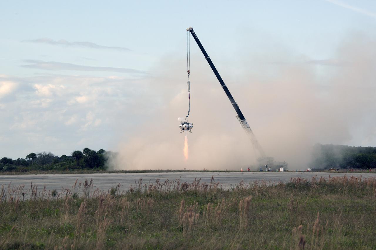 CAPE CANAVERAL, Fla. – At NASA’s Kennedy Space Center in Florida, smoke fills the air as the Project Morpheus prototype lander’s engine fires during a tether test at the north end of the Shuttle Landing Facility. During the test, the lander was lifted 20 feet by crane, and then ascended another 10 feet, maneuvered backwards 10 feet, and then flew forward. It will descend to its original position, landing at the end of the tether onto a transportable launch platform. Testing of the prototype lander was performed at NASA’s Johnson Space Center in Houston in preparation for tethered and free flight testing at Kennedy.    The landing facility will provide the lander with the kind of field necessary for realistic testing, complete with rocks, craters and hazards to avoid. Morpheus utilizes an autonomous landing and hazard avoidance technology, or ALHAT, payload that will allow it to navigate to clear landing sites amidst rocks, craters and other hazards during its descent. Project Morpheus is being managed under the Advanced Exploration Systems, or AES, Division in NASA’s Human Exploration and Operations Mission Directorate. The efforts in AES pioneer new approaches for rapidly developing prototype systems, demonstrating key capabilities and validating operational concepts for future human missions beyond Earth orbit. For more information on Project Morpheus, visit http://morpheuslander.jsc.nasa.gov.  Photo credit: NASA/Daniel Casper