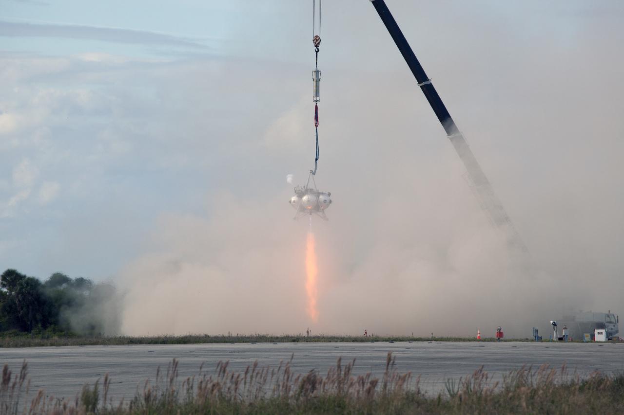 CAPE CANAVERAL, Fla. – At NASA’s Kennedy Space Center in Florida, smoke fills the air as the Project Morpheus prototype lander’s engine fires during a tether test at the north end of the Shuttle Landing Facility. During the test, the lander was lifted 20 feet by crane, and then ascended another 10 feet, maneuvered backwards 10 feet, and then flew forward. It will descend to its original position, landing at the end of the tether onto a transportable launch platform. Testing of the prototype lander was performed at NASA’s Johnson Space Center in Houston in preparation for tethered and free flight testing at Kennedy.    The landing facility will provide the lander with the kind of field necessary for realistic testing, complete with rocks, craters and hazards to avoid. Morpheus utilizes an autonomous landing and hazard avoidance technology, or ALHAT, payload that will allow it to navigate to clear landing sites amidst rocks, craters and other hazards during its descent. Project Morpheus is being managed under the Advanced Exploration Systems, or AES, Division in NASA’s Human Exploration and Operations Mission Directorate. The efforts in AES pioneer new approaches for rapidly developing prototype systems, demonstrating key capabilities and validating operational concepts for future human missions beyond Earth orbit. For more information on Project Morpheus, visit http://morpheuslander.jsc.nasa.gov.  Photo credit: NASA/Daniel Casper