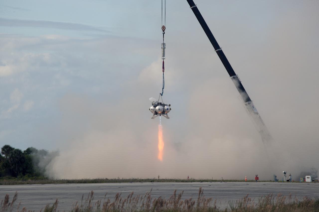 CAPE CANAVERAL, Fla. – At NASA’s Kennedy Space Center in Florida, smoke fills the air as the Project Morpheus prototype lander’s engine fires during a tether test at the north end of the Shuttle Landing Facility. During the test, the lander was lifted 20 feet by crane, and then ascended another 10 feet, maneuvered backwards 10 feet, and then flew forward. It will descend to its original position, landing at the end of the tether onto a transportable launch platform. Testing of the prototype lander was performed at NASA’s Johnson Space Center in Houston in preparation for tethered and free flight testing at Kennedy.    The landing facility will provide the lander with the kind of field necessary for realistic testing, complete with rocks, craters and hazards to avoid. Morpheus utilizes an autonomous landing and hazard avoidance technology, or ALHAT, payload that will allow it to navigate to clear landing sites amidst rocks, craters and other hazards during its descent. Project Morpheus is being managed under the Advanced Exploration Systems, or AES, Division in NASA’s Human Exploration and Operations Mission Directorate. The efforts in AES pioneer new approaches for rapidly developing prototype systems, demonstrating key capabilities and validating operational concepts for future human missions beyond Earth orbit. For more information on Project Morpheus, visit http://morpheuslander.jsc.nasa.gov.  Photo credit: NASA/Daniel Casper