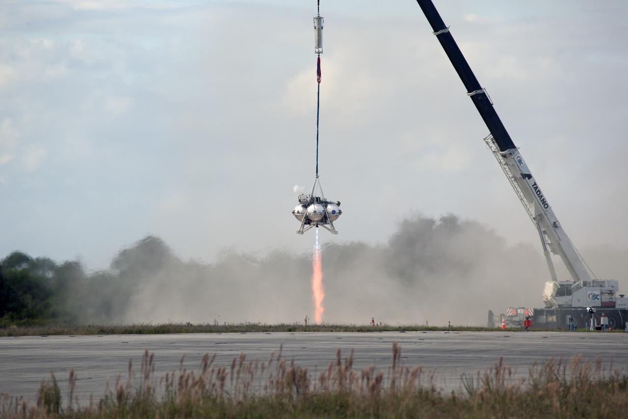 CAPE CANAVERAL, Fla. – At NASA’s Kennedy Space Center in Florida, smoke fills the air as the Project Morpheus prototype lander’s engine fires during a tether test at the north end of the Shuttle Landing Facility. During the test, the lander was lifted 20 feet by crane, and then ascended another 10 feet, maneuvered backwards 10 feet, and then flew forward. It will descend to its original position, landing at the end of the tether onto a transportable launch platform. Testing of the prototype lander was performed at NASA’s Johnson Space Center in Houston in preparation for tethered and free flight testing at Kennedy.    The landing facility will provide the lander with the kind of field necessary for realistic testing, complete with rocks, craters and hazards to avoid. Morpheus utilizes an autonomous landing and hazard avoidance technology, or ALHAT, payload that will allow it to navigate to clear landing sites amidst rocks, craters and other hazards during its descent. Project Morpheus is being managed under the Advanced Exploration Systems, or AES, Division in NASA’s Human Exploration and Operations Mission Directorate. The efforts in AES pioneer new approaches for rapidly developing prototype systems, demonstrating key capabilities and validating operational concepts for future human missions beyond Earth orbit. For more information on Project Morpheus, visit http://morpheuslander.jsc.nasa.gov.  Photo credit: NASA/Daniel Casper