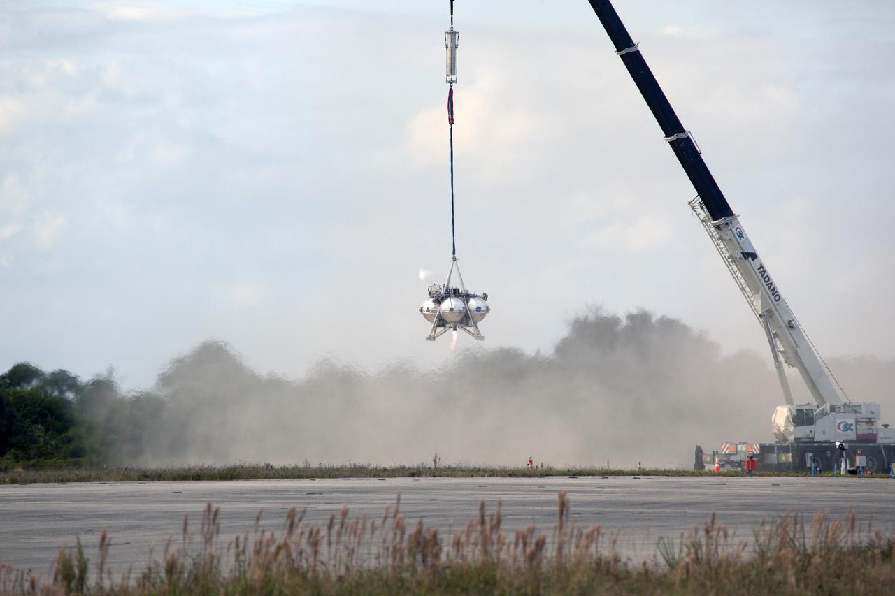 CAPE CANAVERAL, Fla. – At NASA’s Kennedy Space Center in Florida, smoke fills the air as the Project Morpheus prototype lander’s engine fires during a tether test at the north end of the Shuttle Landing Facility. During the test, the lander was lifted 20 feet by crane, and then ascended another 10 feet, maneuvered backwards 10 feet, and then flew forward. It will descend to its original position, landing at the end of the tether onto a transportable launch platform. Testing of the prototype lander was performed at NASA’s Johnson Space Center in Houston in preparation for tethered and free flight testing at Kennedy.    The landing facility will provide the lander with the kind of field necessary for realistic testing, complete with rocks, craters and hazards to avoid. Morpheus utilizes an autonomous landing and hazard avoidance technology, or ALHAT, payload that will allow it to navigate to clear landing sites amidst rocks, craters and other hazards during its descent. Project Morpheus is being managed under the Advanced Exploration Systems, or AES, Division in NASA’s Human Exploration and Operations Mission Directorate. The efforts in AES pioneer new approaches for rapidly developing prototype systems, demonstrating key capabilities and validating operational concepts for future human missions beyond Earth orbit. For more information on Project Morpheus, visit http://morpheuslander.jsc.nasa.gov.  Photo credit: NASA/Daniel Casper