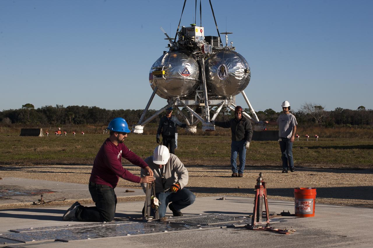 CAPE CANAVERAL, Fla. – Engineers and technicians prepare the launch site for the Project Morpheus prototype lander’s third free flight test at the north end of the Shuttle Landing Facility at NASA’s Kennedy Space Center in Florida. The 57-second test began at 1:15 p.m. EST with the Morpheus lander launching from the ground over a flame trench and ascending about 187 feet, nearly doubling the target ascent velocity from the last test in December 2013. The lander flew forward, covering about 154 feet in 20 seconds before descending and landing within 11 inches of its target on a dedicated pad inside the autonomous landing and hazard avoidance technology, or ALHAT, hazard field. Project Morpheus tests NASA’s ALHAT and an engine that runs on liquid oxygen and methane, or green propellants, into a fully-operational lander that could deliver cargo to other planetary surfaces. The landing facility provides the lander with the kind of field necessary for realistic testing, complete with rocks, craters and hazards to avoid. Morpheus’ ALHAT payload allows it to navigate to clear landing sites amidst rocks, craters and other hazards during its descent. Project Morpheus is being managed under the Advanced Exploration Systems, or AES, Division in NASA’s Human Exploration and Operations Mission Directorate. The efforts in AES pioneer new approaches for rapidly developing prototype systems, demonstrating key capabilities and validating operational concepts for future human missions beyond Earth orbit. For more information on Project Morpheus, visit http://www.nasa.gov/centers/johnson/exploration/morpheus. Photo credit: NASA/Kim Shiflett  