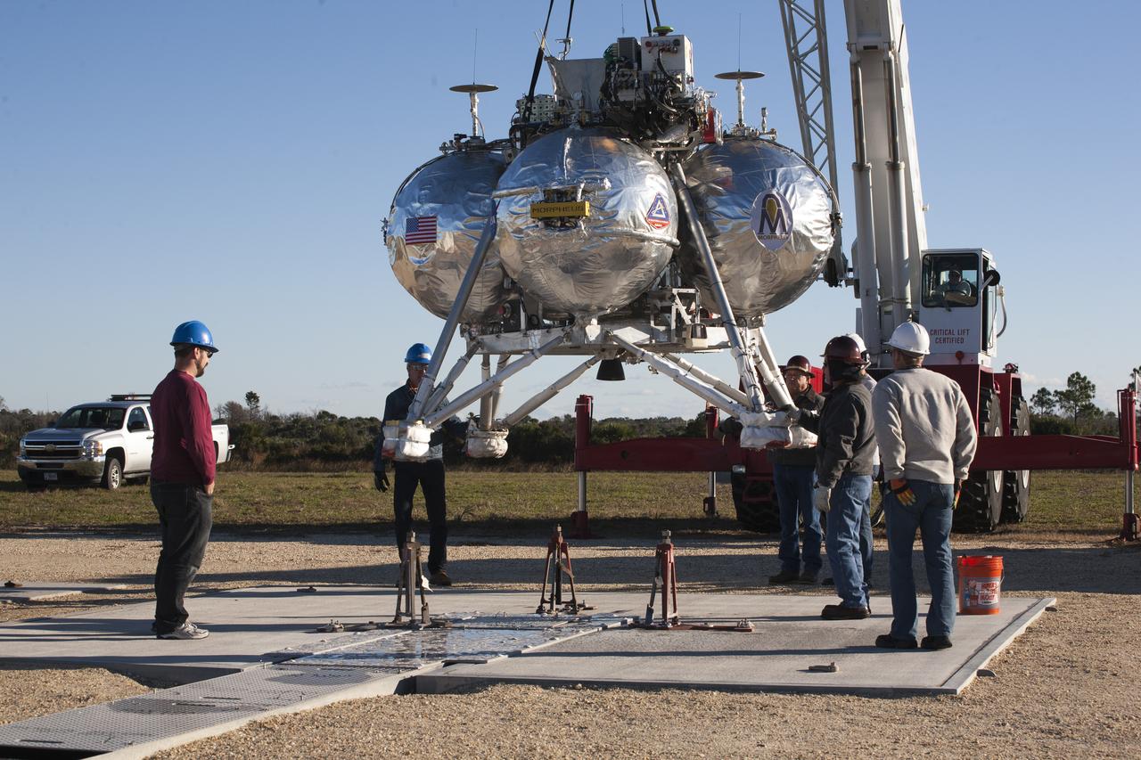 CAPE CANAVERAL, Fla. – Engineers and technicians monitor the progress as the Project Morpheus prototype lander is lowered onto the launch site for its third free flight test at the north end of the Shuttle Landing Facility at NASA’s Kennedy Space Center in Florida. The 57-second test began at 1:15 p.m. EST with the Morpheus lander launching from the ground over a flame trench and ascending about 187 feet, nearly doubling the target ascent velocity from the last test in December 2013. The lander flew forward, covering about 154 feet in 20 seconds before descending and landing within 11 inches of its target on a dedicated pad inside the autonomous landing and hazard avoidance technology, or ALHAT, hazard field. Project Morpheus tests NASA’s ALHAT and an engine that runs on liquid oxygen and methane, or green propellants, into a fully-operational lander that could deliver cargo to other planetary surfaces. The landing facility provides the lander with the kind of field necessary for realistic testing, complete with rocks, craters and hazards to avoid. Morpheus’ ALHAT payload allows it to navigate to clear landing sites amidst rocks, craters and other hazards during its descent. Project Morpheus is being managed under the Advanced Exploration Systems, or AES, Division in NASA’s Human Exploration and Operations Mission Directorate. The efforts in AES pioneer new approaches for rapidly developing prototype systems, demonstrating key capabilities and validating operational concepts for future human missions beyond Earth orbit. For more information on Project Morpheus, visit http://www.nasa.gov/centers/johnson/exploration/morpheus. Photo credit: NASA/Kim Shiflett