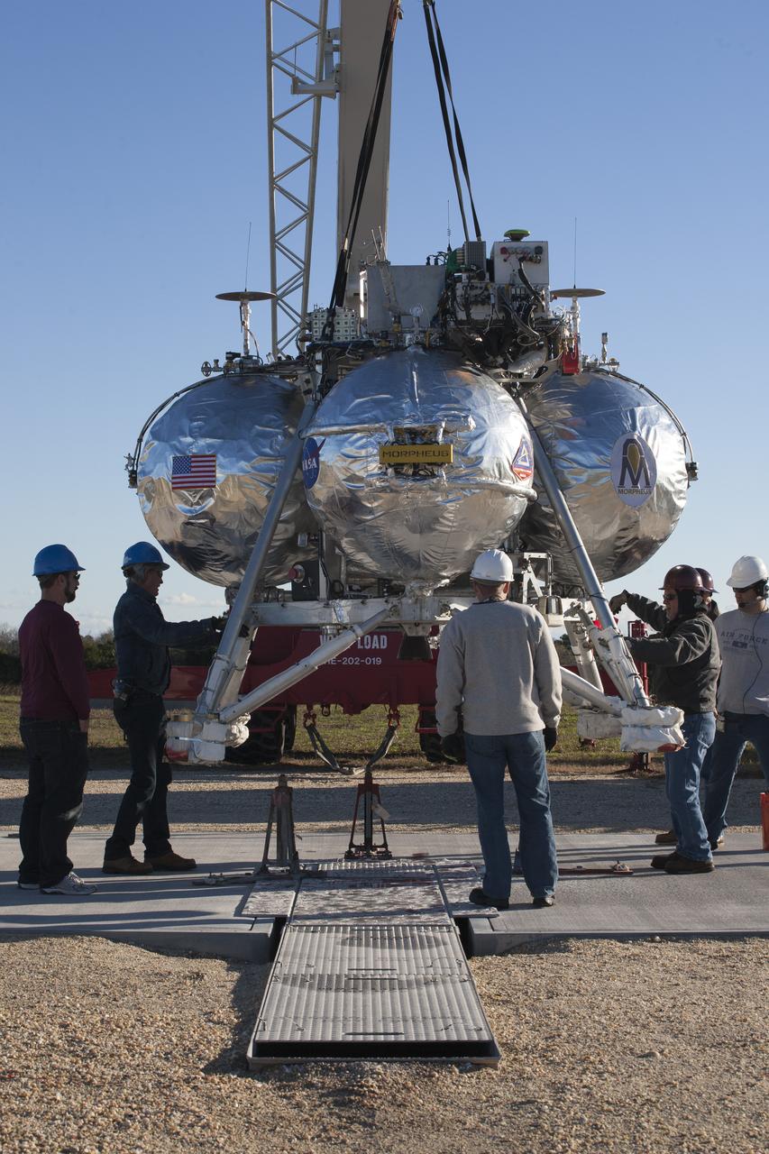 CAPE CANAVERAL, Fla. – Engineers and technicians monitor the progress as the Project Morpheus prototype lander is lowered onto the launch site for its third free flight test at the north end of the Shuttle Landing Facility at NASA’s Kennedy Space Center in Florida. The 57-second test began at 1:15 p.m. EST with the Morpheus lander launching from the ground over a flame trench and ascending about 187 feet, nearly doubling the target ascent velocity from the last test in December 2013. The lander flew forward, covering about 154 feet in 20 seconds before descending and landing within 11 inches of its target on a dedicated pad inside the autonomous landing and hazard avoidance technology, or ALHAT, hazard field. Project Morpheus tests NASA’s ALHAT and an engine that runs on liquid oxygen and methane, or green propellants, into a fully-operational lander that could deliver cargo to other planetary surfaces. The landing facility provides the lander with the kind of field necessary for realistic testing, complete with rocks, craters and hazards to avoid. Morpheus’ ALHAT payload allows it to navigate to clear landing sites amidst rocks, craters and other hazards during its descent. Project Morpheus is being managed under the Advanced Exploration Systems, or AES, Division in NASA’s Human Exploration and Operations Mission Directorate. The efforts in AES pioneer new approaches for rapidly developing prototype systems, demonstrating key capabilities and validating operational concepts for future human missions beyond Earth orbit. For more information on Project Morpheus, visit http://www.nasa.gov/centers/johnson/exploration/morpheus. Photo credit: NASA/Kim Shiflett