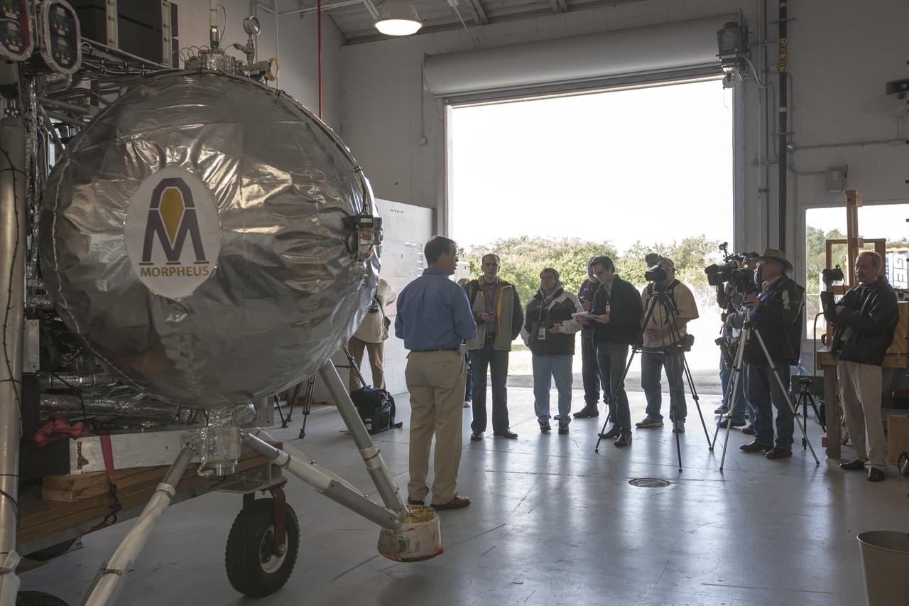 CAPE CANAVERAL, Fla. – Members of the news media view the Project Morpheus prototype lander inside a hangar near the Shuttle Landing Facility at NASA’s Kennedy Space Center in Florida. Speaking to the media is Greg Gaddis, the Kennedy Morpheus and ALHAT site manager. Morpheus successfully completed its third free flight test Jan. 16. The 57-second test began at 1:15 p.m. EST with the Morpheus lander launching from the ground over a flame trench and ascending about 187 feet, nearly doubling the target ascent velocity from the last test in December 2013. The lander flew forward, covering about 154 feet in 20 seconds before descending and landing within 11 inches of its target on a dedicated pad inside the autonomous landing and hazard avoidance technology, or ALHAT, hazard field. Project Morpheus tests NASA’s ALHAT and an engine that runs on liquid oxygen and methane, or green propellants, into a fully-operational lander that could deliver cargo to other planetary surfaces. The landing facility provides the lander with the kind of field necessary for realistic testing, complete with rocks, craters and hazards to avoid. Morpheus’ ALHAT payload allows it to navigate to clear landing sites amidst rocks, craters and other hazards during its descent. Project Morpheus is being managed under the Advanced Exploration Systems, or AES, Division in NASA’s Human Exploration and Operations Mission Directorate. The efforts in AES pioneer new approaches for rapidly developing prototype systems, demonstrating key capabilities and validating operational concepts for future human missions beyond Earth orbit. For more information on Project Morpheus, visit http://www.nasa.gov/centers/johnson/exploration/morpheus. Photo credit: NASA/Kim Shiflett