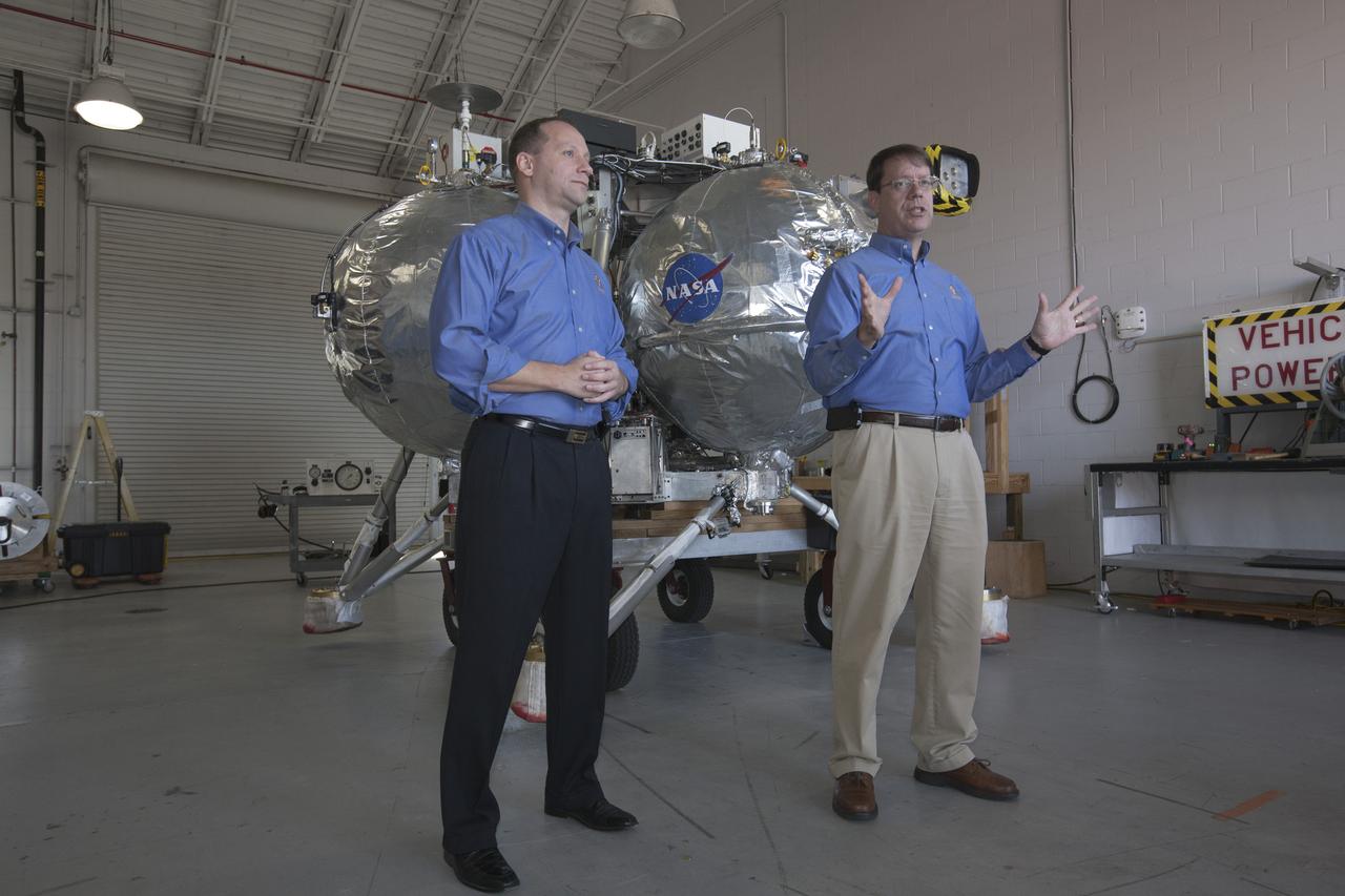 CAPE CANAVERAL, Fla. – Members of the news media view the Project Morpheus prototype lander inside a hangar near the Shuttle Landing Facility at NASA’s Kennedy Space Center in Florida. Speaking to the media, from left are Jon Olansen, Morpheus project manager at Johnson Space Center in Houston, and Greg Gaddis, the Kennedy Morpheus and ALHAT site manager. Morpheus successfully completed its third free flight test Jan. 16. The 57-second test began at 1:15 p.m. EST with the Morpheus lander launching from the ground over a flame trench and ascending about 187 feet, nearly doubling the target ascent velocity from the last test in December 2013. The lander flew forward, covering about 154 feet in 20 seconds before descending and landing within 11 inches of its target on a dedicated pad inside the autonomous landing and hazard avoidance technology, or ALHAT, hazard field. Project Morpheus tests NASA’s ALHAT and an engine that runs on liquid oxygen and methane, or green propellants, into a fully-operational lander that could deliver cargo to other planetary surfaces. The landing facility provides the lander with the kind of field necessary for realistic testing, complete with rocks, craters and hazards to avoid. Morpheus’ ALHAT payload allows it to navigate to clear landing sites amidst rocks, craters and other hazards during its descent. Project Morpheus is being managed under the Advanced Exploration Systems, or AES, Division in NASA’s Human Exploration and Operations Mission Directorate. The efforts in AES pioneer new approaches for rapidly developing prototype systems, demonstrating key capabilities and validating operational concepts for future human missions beyond Earth orbit. For more information on Project Morpheus, visit http://www.nasa.gov/centers/johnson/exploration/morpheus. Photo credit: NASA/Kim Shiflett