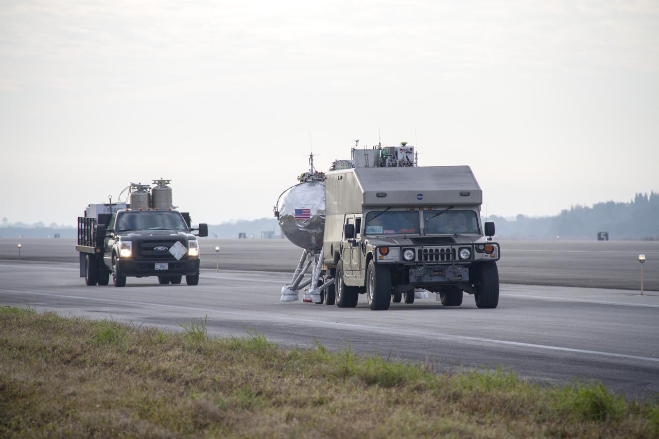 CAPE CANAVERAL, Fla. – The Project Morpheus prototype lander is transported to a launch pad at the north end of the Shuttle Landing Facility at NASA’s Kennedy Space Center in Florida. The prototype lander is being prepared for its fourth free flight test at Kennedy. Morpheus will launch from the ground over a flame trench and then descend and land on a dedicated pad inside the autonomous landing and hazard avoidance technology, or ALHAT, hazard field. Project Morpheus tests NASA’s ALHAT and an engine that runs on liquid oxygen and methane, or green propellants, into a fully-operational lander that could deliver cargo to other planetary surfaces. The landing facility provides the lander with the kind of field necessary for realistic testing, complete with rocks, craters and hazards to avoid. Morpheus’ ALHAT payload allows it to navigate to clear landing sites amidst rocks, craters and other hazards during its descent. Project Morpheus is being managed under the Advanced Exploration Systems, or AES, Division in NASA’s Human Exploration and Operations Mission Directorate. The efforts in AES pioneer new approaches for rapidly developing prototype systems, demonstrating key capabilities and validating operational concepts for future human missions beyond Earth orbit. For more information on Project Morpheus, visit http://www.nasa.gov/centers/johnson/exploration/morpheus. Photo credit: NASA/Cory Huston  