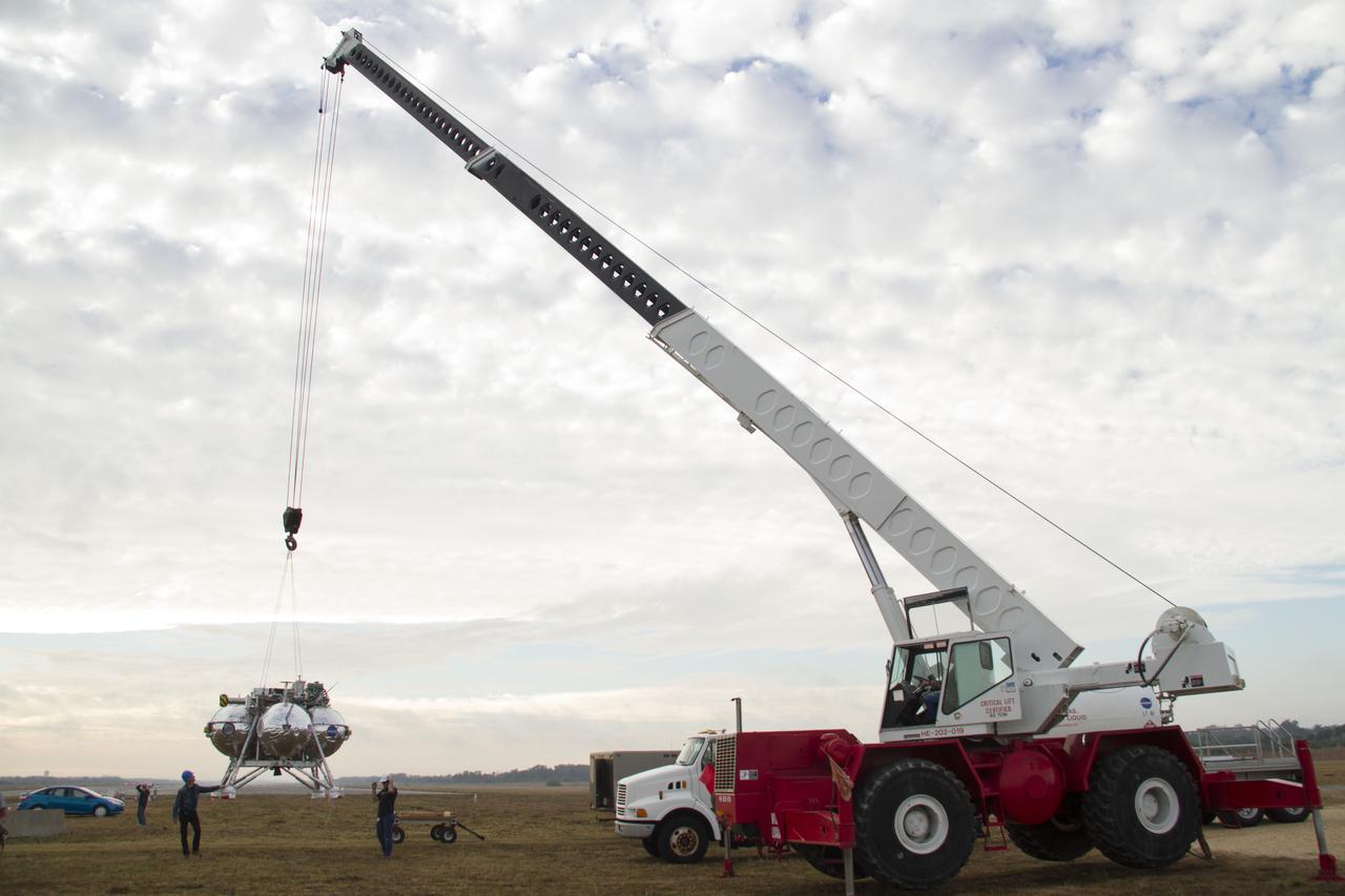 CAPE CANAVERAL, Fla. – The Project Morpheus prototype lander is being lifted by crane for positioning on a launch pad at the north end of the Shuttle Landing Facility at NASA’s Kennedy Space Center in Florida. The prototype lander is being prepared for its fourth free flight test at Kennedy. Morpheus will launch from the ground over a flame trench and then descend and land on a dedicated pad inside the autonomous landing and hazard avoidance technology, or ALHAT, hazard field. Project Morpheus tests NASA’s ALHAT and an engine that runs on liquid oxygen and methane, or green propellants, into a fully-operational lander that could deliver cargo to other planetary surfaces. The landing facility provides the lander with the kind of field necessary for realistic testing, complete with rocks, craters and hazards to avoid. Morpheus’ ALHAT payload allows it to navigate to clear landing sites amidst rocks, craters and other hazards during its descent. Project Morpheus is being managed under the Advanced Exploration Systems, or AES, Division in NASA’s Human Exploration and Operations Mission Directorate. The efforts in AES pioneer new approaches for rapidly developing prototype systems, demonstrating key capabilities and validating operational concepts for future human missions beyond Earth orbit. For more information on Project Morpheus, visit http://www.nasa.gov/centers/johnson/exploration/morpheus. Photo credit: NASA/Cory Huston
