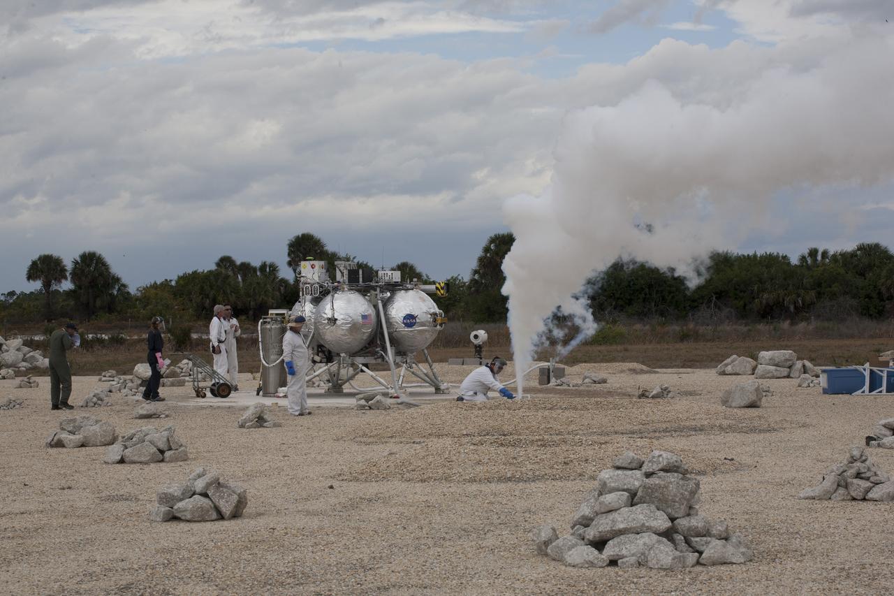 CAPE CANAVERAL, Fla. – Technicians and engineers perform safing procedures on the Project Morpheus prototype lander after it touched down in the autonomous landing and hazard avoidance technology, or ALHAT, hazard field. The lander successfully completed its fourth free flight test at the north end of the Shuttle Landing Facility at NASA’s Kennedy Space Center in Florida. The 64-second test began at 1:15 p.m. EST with the Morpheus lander launching from the ground over a flame trench and ascending about 305 feet, significantly increasing the ascent velocity from the last test. The lander flew forward, covering about 358 feet in 25 seconds before descending and landing within 15 inches of its target on a dedicated pad inside the ALHAT hazard field. Project Morpheus tests NASA’s ALHAT and an engine that runs on liquid oxygen and methane, or green propellants, into a fully-operational lander that could deliver cargo to other planetary surfaces. The landing facility provides the lander with the kind of field necessary for realistic testing, complete with rocks, craters and hazards to avoid. Morpheus’ ALHAT payload allows it to navigate to clear landing sites amidst rocks, craters and other hazards during its descent. Project Morpheus is being managed under the Advanced Exploration Systems, or AES, Division in NASA’s Human Exploration and Operations Mission Directorate. The efforts in AES pioneer new approaches for rapidly developing prototype systems, demonstrating key capabilities and validating operational concepts for future human missions beyond Earth orbit. For more information on Project Morpheus, visit http://www.nasa.gov/centers/johnson/exploration/morpheus. Photo credit: NASA/Kim Shiflett  