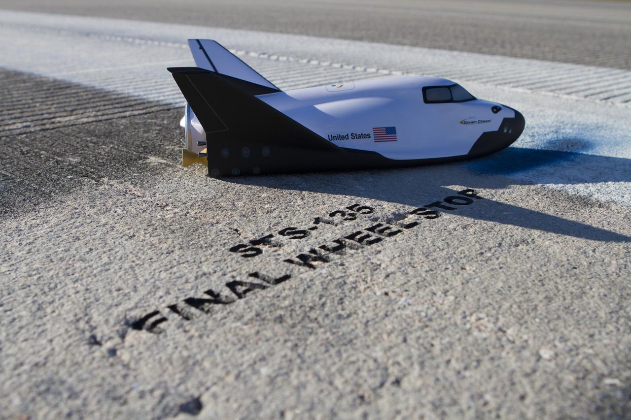 CAPE CANAVERAL, Fla. – A model of the Sierra Nevada Corporation, or SNC, Dream Chaser spacecraft stands next to the final wheelstop location of space shuttle Atlantis, the final shuttle to land on the 3.5-mile-long runway at Kennedy Space Center’s Shuttle Landing Facility. SNC announced it plans to work with United Launch Alliance, or ULA, to launch the Dream Chaser spacecraft into orbit atop an Atlas V rocket from Space Launch Complex 41 at Cape Canaveral Air Force Station in November 2016 intends to land the winged spacecraft at the Shuttle Landing Facility lease office space at Exploration Park, right outside Kennedy’s gates and process the spacecraft in the high bay of the Operations and Checkout Building at Kennedy, with Lockheed Martin performing the work. The announcements made during a news conference at Kennedy are considered substantial for SNC and important to plans by NASA and Space Florida for Kennedy’s transformation into a multi-user spaceport for both commercial and government customers. Photo credit: NASA/Cory Huston