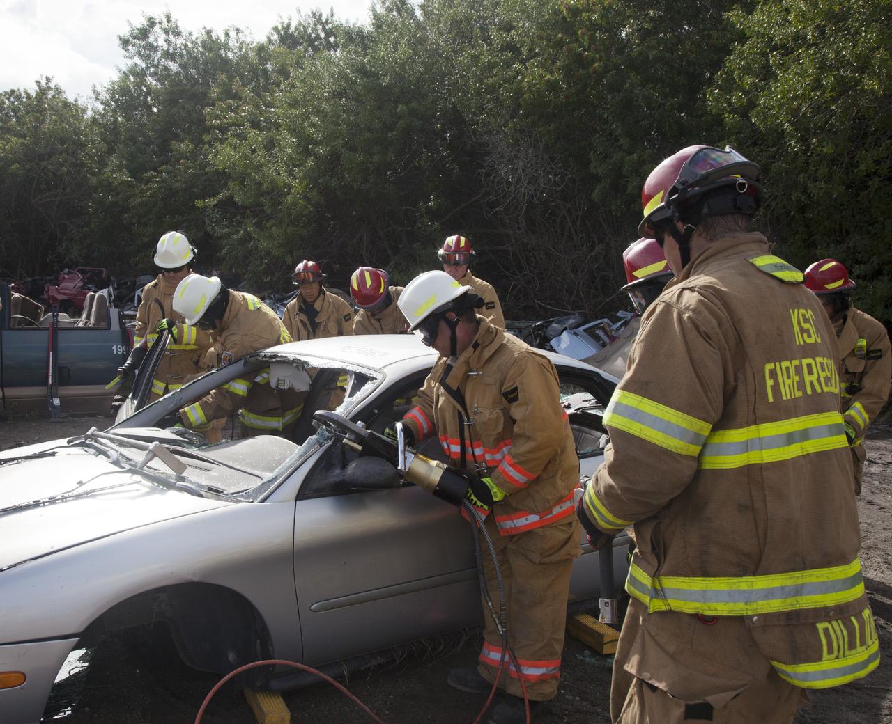 CAPE CANAVERAL, Fla. – Special Rescue Operations firefighters with NASA Fire Rescue Services in the Protective Services Office at NASA’s Kennedy Space Center in Florida practice vehicle extrication training at an auto salvage yard near the center. A firefighter uses a special hydraulic tool to cut through a section of the car to remove the roof, while other firefighters clear the windows and prepare to use the Jaws of Life to simulate the rescue of a trapped and injured person. Other rescue equipment being used includes axes and tools to punch through and clear away windshields and windows.     Kennedy’s firefighters recently achieved Pro Board Certification in aerial fire truck operations. With the completion of vehicle extrication and Jaws of Life training, the Protective Services Office is one step closer to achieving certification in vehicle machinery extrication. Kennedy’s firefighters are with G4S Government Solutions Inc., on the Kennedy Protective Services Contract. Photo credit: NASA/Daniel Casper