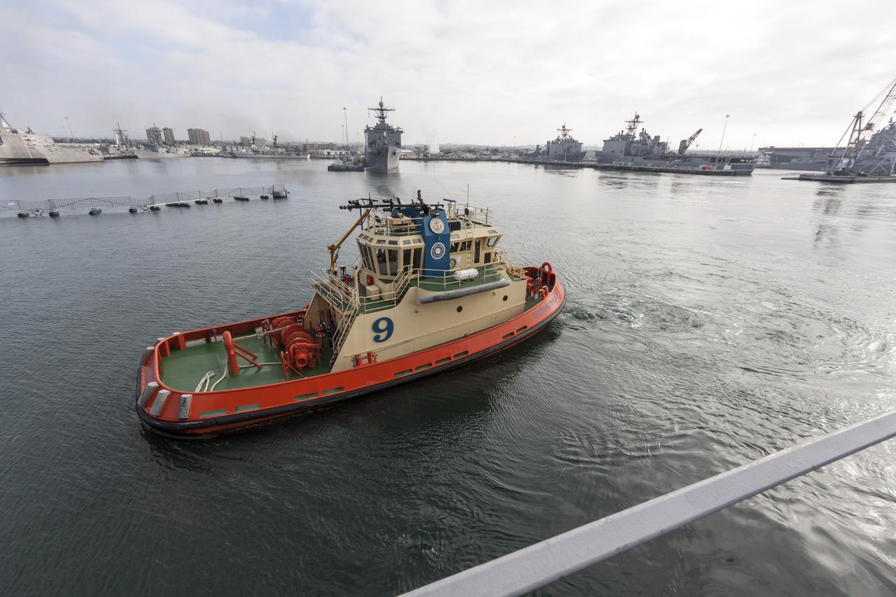 SAN DIEGO, Calif. – At the U.S. Naval Base San Diego in California, a tug boat accompanies the USS San Diego as it departs for open seas in the Pacific Ocean. The Orion boilerplate test vehicle and other support equipment are secured in the ship’s well deck in preparation for an underway recovery test about 100 miles offshore. NASA and the U.S. Navy conducted tests to prepare for recovery of the Orion crew module, forward bay cover and parachutes on its return from a deep space mission. The underway recovery test will allow the teams to demonstrate and evaluate the recovery processes, procedures, hardware and personnel in open waters. During the testing, the tether lines were unable to support the tension caused by crew module motion that was driven by wave turbulence in the well deck of the ship. NASA and the U.S. Navy are reviewing the testing data collected to evaluate the next steps. The Ground Systems Development and Operations Program conducted the underway recovery tests. Orion is the exploration spacecraft designed to carry astronauts to destinations not yet explored by humans, including an asteroid and Mars. It will have emergency abort capability, sustain the crew during space travel and provide safe re-entry from deep space return velocities. The first unpiloted test flight of the Orion is scheduled to launch in 2014 atop a Delta IV rocket and in 2017 on NASA’s Space Launch System rocket. For more information, visit http://www.nasa.gov/orion. Photo credit: NASA/Cory Huston  