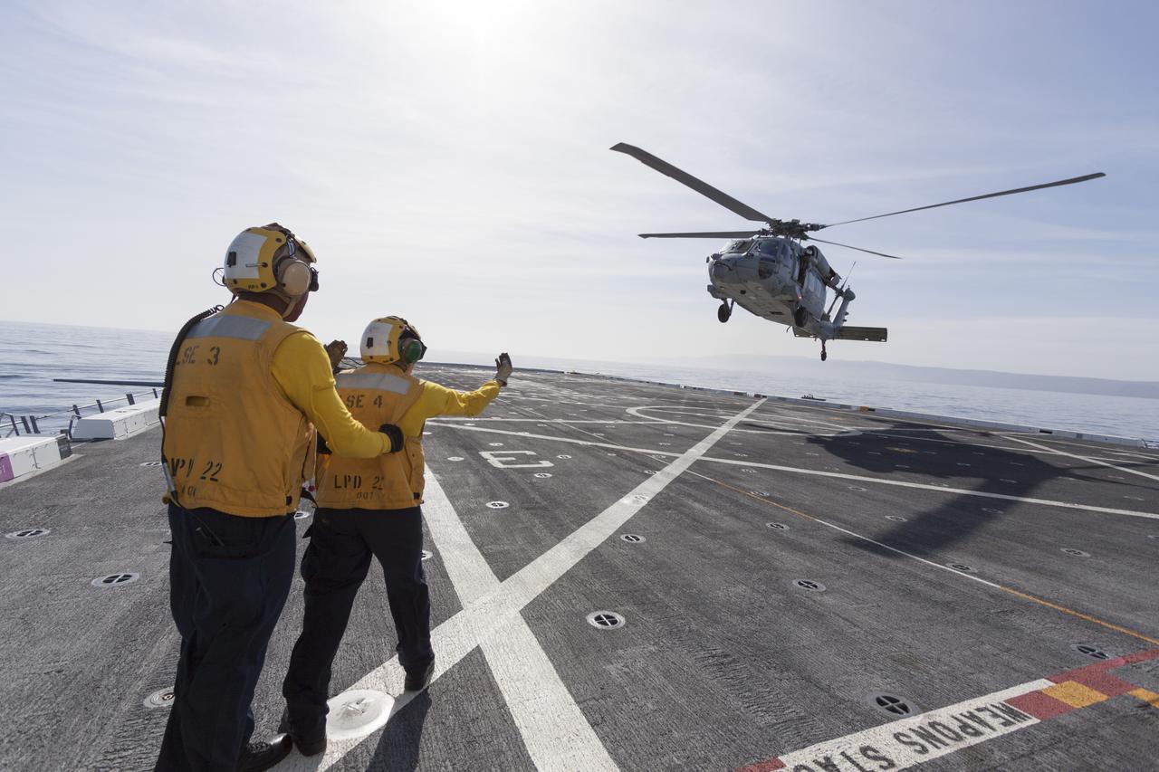 SAN DIEGO, Calif. – On the top deck of the USS San Diego, U.S. Navy personnel monitor a helicopter landing after an Orion underway recovery test. The Orion boilerplate test vehicle and other hardware were secured in the well deck of the USS San Diego at the U.S. Naval Base San Diego in California. Orion was transported about 100 miles offshore for an underway recovery test. NASA and the U.S. Navy conducted tests to prepare for recovery of the Orion crew module, forward bay cover and parachutes on its return from a deep space mission. The underway recovery test allowed the teams to demonstrate and evaluate the recovery processes, procedures, hardware and personnel in open waters. During the testing, the tether lines were unable to support the tension caused by crew module motion that was driven by wave turbulence in the well deck of the ship. NASA and the U.S. Navy are reviewing the testing data collected to evaluate the next steps. The Ground Systems Development and Operations Program conducted the underway recovery tests. Orion is the exploration spacecraft designed to carry astronauts to destinations not yet explored by humans, including an asteroid and Mars. It will have emergency abort capability, sustain the crew during space travel and provide safe re-entry from deep space return velocities. The first unpiloted test flight of the Orion is scheduled to launch in 2014 atop a Delta IV rocket and in 2017 on NASA’s Space Launch System rocket. For more information, visit http://www.nasa.gov/orion. Photo credit: NASA/Cory Huston