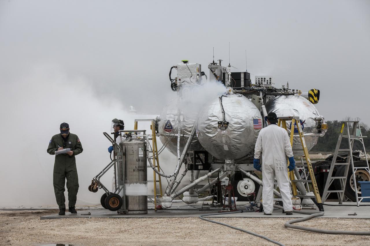 CAPE CANAVERAL, Fla. – Engineers and technicians prepare the Project Morpheus prototype lander for its sixth free flight test from a launch pad at the north end of the Shuttle Landing Facility at NASA’s Kennedy Space Center in Florida. The 82-second test began at 11:32 a.m. EST with the Morpheus lander launching from the ground over a flame trench and ascending to 465 feet. The lander flew forward, covering 633 feet while performing a 55-foot divert to emulate a hazard avoidance maneuver before descending and landing on a dedicated pad inside the automated landing and hazard avoidance technology, or ALHAT, hazard field. Morpheus landed 10 inches west of its intended target. Project Morpheus tests NASA’s ALHAT and an engine that runs on liquid oxygen and methane, or green propellants, into a fully-operational lander that could deliver cargo to other planetary surfaces. The landing facility provides the lander with the kind of field necessary for realistic testing, complete with rocks, craters and hazards to avoid. Morpheus’ ALHAT payload allows it to navigate to clear landing sites amidst rocks, craters and other hazards during its descent. Project Morpheus is being managed under the Advanced Exploration Systems, or AES, Division in NASA’s Human Exploration and Operations Mission Directorate. The efforts in AES pioneer new approaches for rapidly developing prototype systems, demonstrating key capabilities and validating operational concepts for future human missions beyond Earth orbit. For more information on Project Morpheus, visit http://morpheuslander.jsc.nasa.gov/. Photo credit: NASA/Kim Shiflett