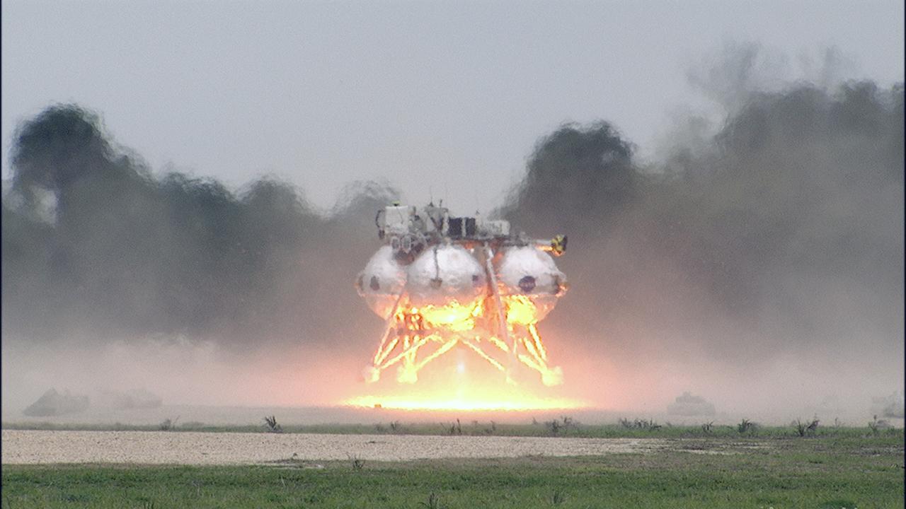CAPE CANAVERAL, Fla. – The Project Morpheus prototype lander touches down in the automated landing and hazard avoidance technology, or ALHAT, hazard field after completing its sixth free flight test at the north end of the Shuttle Landing Facility at NASA’s Kennedy Space Center in Florida. The 82-second test began at 11:32 a.m. EST with the Morpheus lander launching from the ground over a flame trench and ascending to 465 feet. The lander flew forward, covering 633 feet while performing a 55-foot divert to emulate a hazard avoidance maneuver before descending and landing on a dedicated pad inside the hazard field. Morpheus landed 10 inches west of its intended target. Project Morpheus tests NASA’s ALHAT and an engine that runs on liquid oxygen and methane, or green propellants, into a fully-operational lander that could deliver cargo to other planetary surfaces. The landing facility provides the lander with the kind of field necessary for realistic testing, complete with rocks, craters and hazards to avoid. Morpheus’ ALHAT payload allows it to navigate to clear landing sites amidst rocks, craters and other hazards during its descent. Project Morpheus is being managed under the Advanced Exploration Systems, or AES, Division in NASA’s Human Exploration and Operations Mission Directorate. The efforts in AES pioneer new approaches for rapidly developing prototype systems, demonstrating key capabilities and validating operational concepts for future human missions beyond Earth orbit. For more information on Project Morpheus, visit http://morpheuslander.jsc.nasa.gov/. Photo credit: NASA/Frankie Martin
