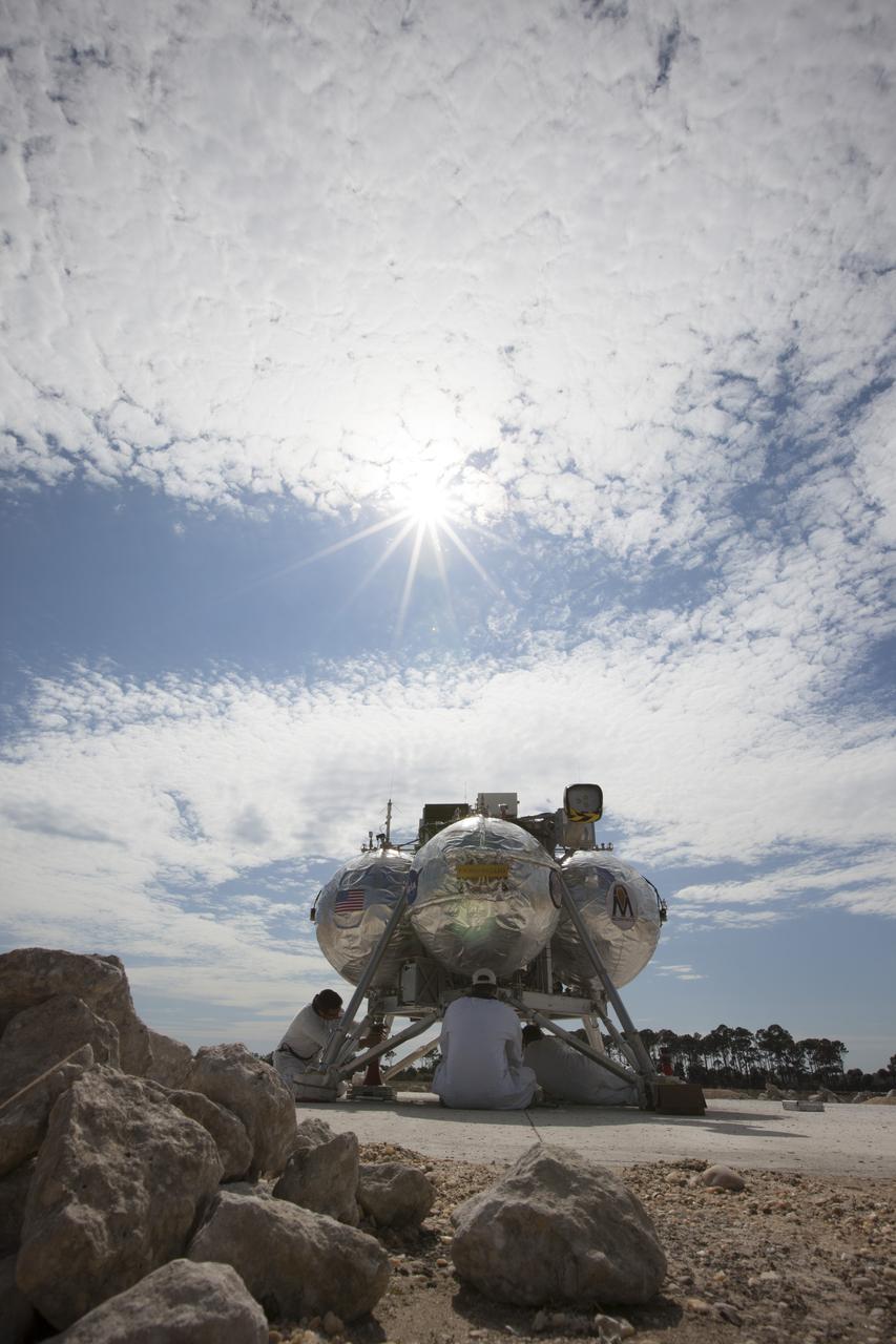 CAPE CANAVERAL, Fla. - Technicians prepare the Project Morpheus prototype lander for its seventh free flight test at the north end of the Shuttle Landing Facility at NASA’s Kennedy Space Center in Florida. The 83-second test began at 3:41 p.m. EDT with the Morpheus lander launching from the ground over a flame trench and ascending to 580 feet, its highest to date. Morpheus then flew its fastest downrange trek at 30 mph, travelling farther than before, 837 feet. The lander performed a 42-foot divert to emulate a hazard avoidance maneuver before descending and touching down on Landing Site 2, at the northern landing pad inside the automated landing and hazard avoidance technology ALHAT hazard field. Morpheus landed within one foot of its intended target. Project Morpheus tests NASA’s ALHAT and an engine that runs on liquid oxygen and methane, or green propellants, into a fully-operational lander that could deliver cargo to other planetary surfaces. The landing facility provides the lander with the kind of field necessary for realistic testing, complete with rocks, craters and hazards to avoid. Morpheus’ ALHAT payload allows it to navigate to clear landing sites amidst rocks, craters and other hazards during its descent. Project Morpheus is being managed under the Advanced Exploration Systems, or AES, Division in NASA’s Human Exploration and Operations Mission Directorate. The efforts in AES pioneer new approaches for rapidly developing prototype systems, demonstrating key capabilities and validating operational concepts for future human missions beyond Earth orbit. For more information on Project Morpheus, visit http://morpheuslander.jsc.nasa.gov/. Photo credit: NASA/Kim Shiflett