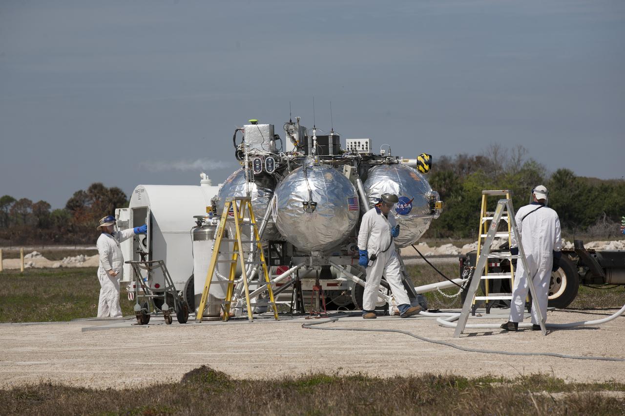 CAPE CANAVERAL, Fla. - Engineers and technicians prepare the Project Morpheus prototype lander for its seventh free flight test at the north end of the Shuttle Landing Facility at NASA’s Kennedy Space Center in Florida. The 83-second test began at 3:41 p.m. EDT with the Morpheus lander launching from the ground over a flame trench and ascending to 580 feet, its highest to date. Morpheus then flew its fastest downrange trek at 30 mph, travelling farther than before, 837 feet. The lander performed a 42-foot divert to emulate a hazard avoidance maneuver before descending and touching down on Landing Site 2, at the northern landing pad inside the automated landing and hazard avoidance technology ALHAT hazard field. Morpheus landed within one foot of its intended target. Project Morpheus tests NASA’s ALHAT and an engine that runs on liquid oxygen and methane, or green propellants, into a fully-operational lander that could deliver cargo to other planetary surfaces. The landing facility provides the lander with the kind of field necessary for realistic testing, complete with rocks, craters and hazards to avoid. Morpheus’ ALHAT payload allows it to navigate to clear landing sites amidst rocks, craters and other hazards during its descent. Project Morpheus is being managed under the Advanced Exploration Systems, or AES, Division in NASA’s Human Exploration and Operations Mission Directorate. The efforts in AES pioneer new approaches for rapidly developing prototype systems, demonstrating key capabilities and validating operational concepts for future human missions beyond Earth orbit. For more information on Project Morpheus, visit http://morpheuslander.jsc.nasa.gov/. Photo credit: NASA/Kim Shiflett