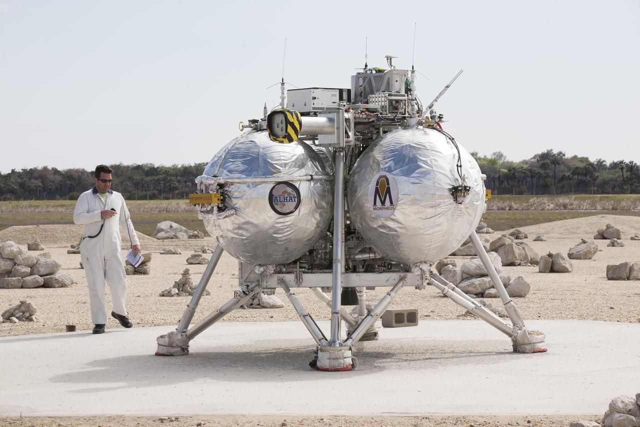 CAPE CANAVERAL, Fla. - An engineer checks the Project Morpheus prototype lander after it landed in the automated landing and hazard avoidance technology, or ALHAT, hazard field, completing its seventh free flight test at the north end of the Shuttle Landing Facility at NASA’s Kennedy Space Center in Florida. The 83-second test began at 3:41 p.m. EDT with the Morpheus lander launching from the ground over a flame trench and ascending to 580 feet, its highest to date. Morpheus then flew its fastest downrange trek at 30 mph, travelling farther than before, 837 feet. The lander performed a 42-foot divert to emulate a hazard avoidance maneuver before descending and touching down on Landing Site 2, at the northern landing pad inside the hazard field. Morpheus landed within one foot of its intended target. Project Morpheus tests NASA’s ALHAT and an engine that runs on liquid oxygen and methane, or green propellants, into a fully-operational lander that could deliver cargo to other planetary surfaces. The landing facility provides the lander with the kind of field necessary for realistic testing, complete with rocks, craters and hazards to avoid. Morpheus’ ALHAT payload allows it to navigate to clear landing sites amidst rocks, craters and other hazards during its descent. Project Morpheus is being managed under the Advanced Exploration Systems, or AES, Division in NASA’s Human Exploration and Operations Mission Directorate. The efforts in AES pioneer new approaches for rapidly developing prototype systems, demonstrating key capabilities and validating operational concepts for future human missions beyond Earth orbit. For more information on Project Morpheus, visit http://morpheuslander.jsc.nasa.gov/. Photo credit: NASA/Kim Shiflett