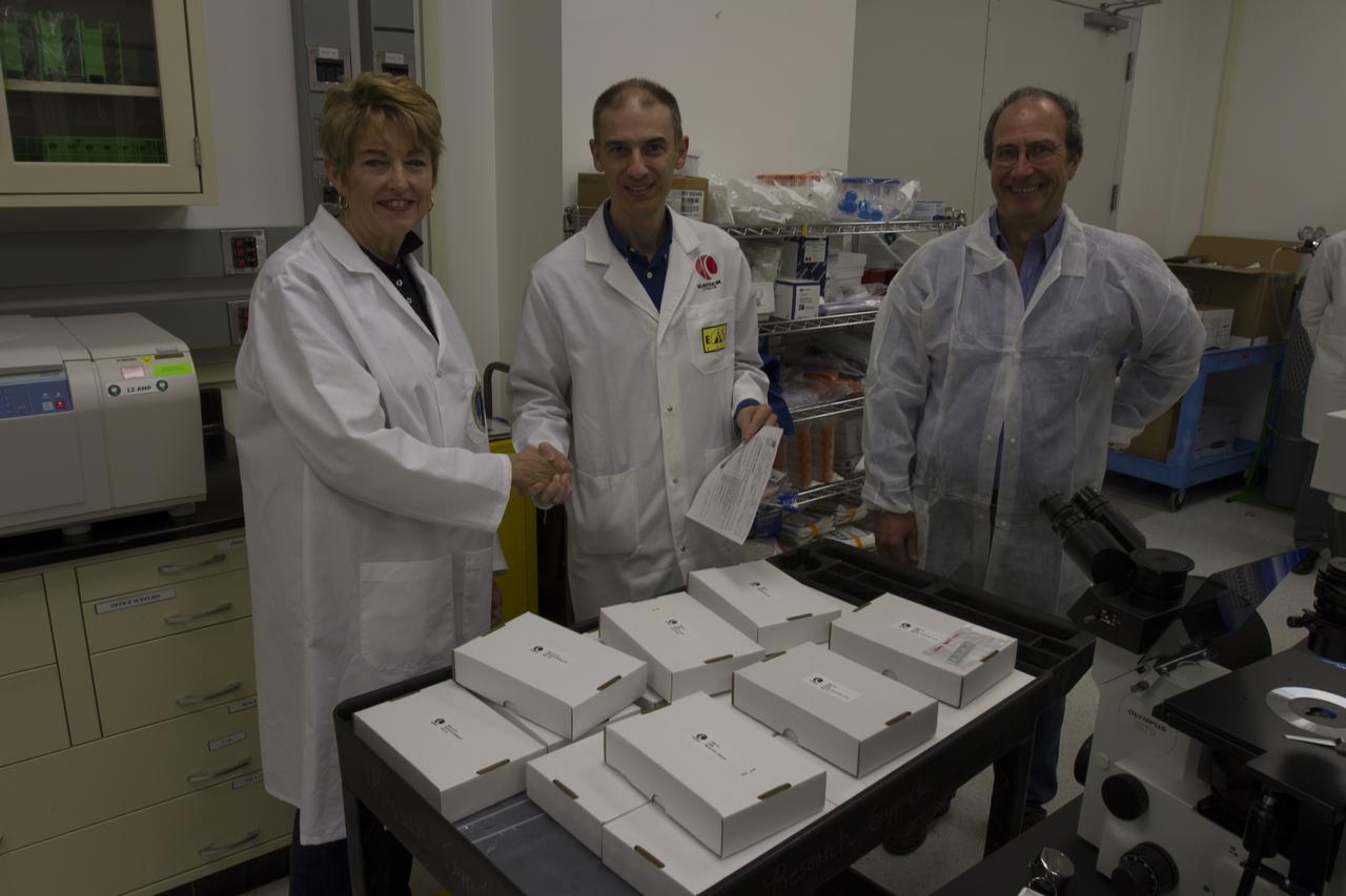CAPE CANAVERAL, Fla. - Researcher and former NASA payload specialist Millie Hughes-Fulford, of the Hughes-Fulford Laboratory, San Francisco, Calif., accepts the European Space Agency ESA T-cell experiment flight units being handed over in a Space Station Processing Facility laboratory at NASA's Kennedy Space Center in Florida. From left are Hughes-Fulford shaking hands with Pier Luigi Ganga of Kayser Italia, manufacturer of the hardware, with Raimondo Fortezza of ESA looking on. The immunology experiment will launch on SpaceX-3 and focus on the effects of microgravity on early T-cell signaling pathways. Current work aims to identify and compare the gene expression of microRNAs miRNAs during T-cell activation under normal gravity and in microgravity, and compare those patterns to changes seen in aging populations. The experiment will be the first flown on SpaceX funded by the National Institutes of Health. Dr. Hughes-Fulford flew aboard space shuttle mission STS-40 in June 1991, the first Spacelab mission dedicated to biomedical studies. For more information on the T-cell experiment, visit http://hughesfulfordlab.com and http://www.nasa.gov/ames/research/space-biosciences/t-cell-activation-in-aging-spacex-3/. Photo credit: NASA/Cory Huston
